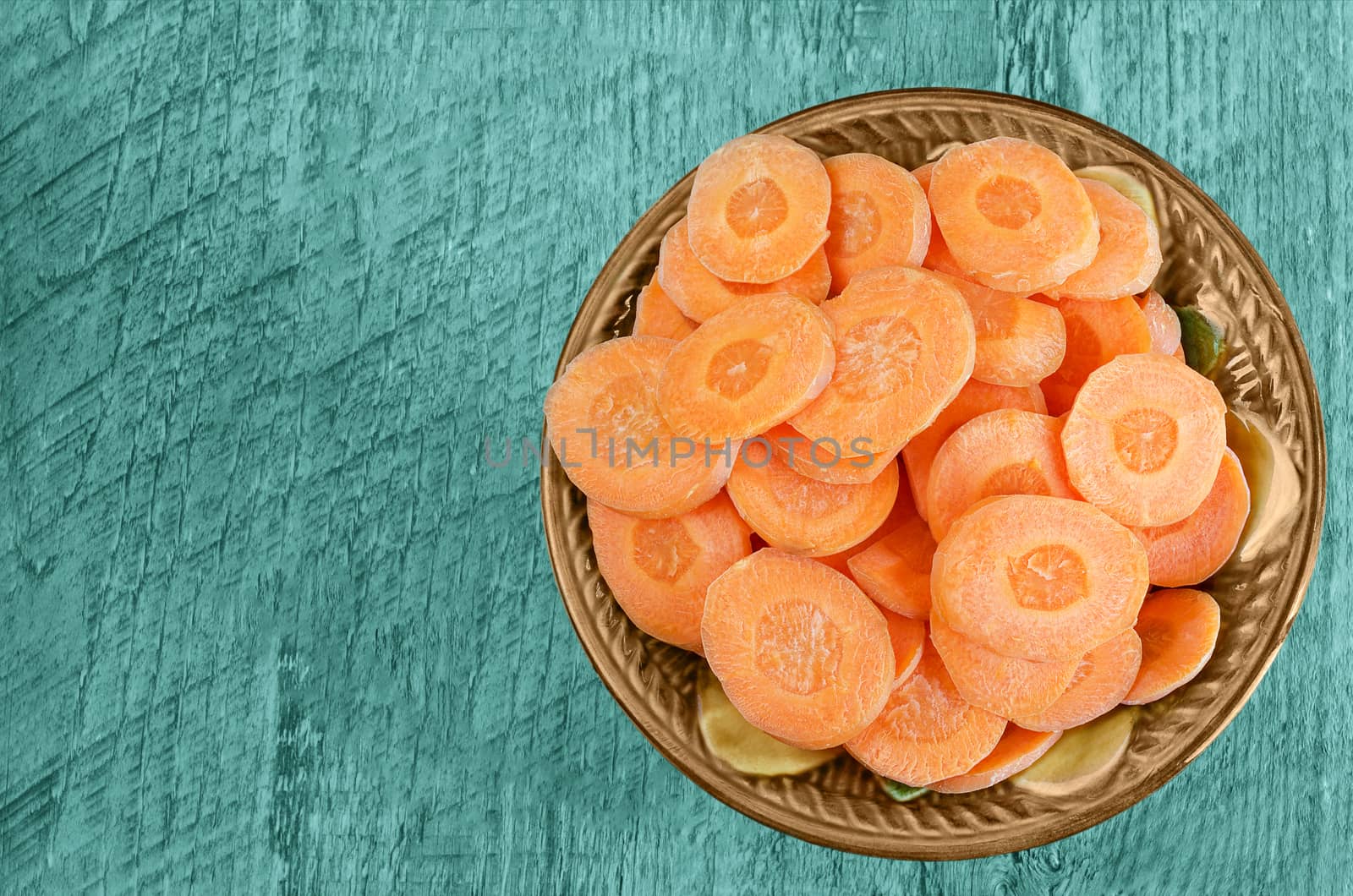 Sliced carrots in a bowl on wooden background. Tinted in blue-green color.