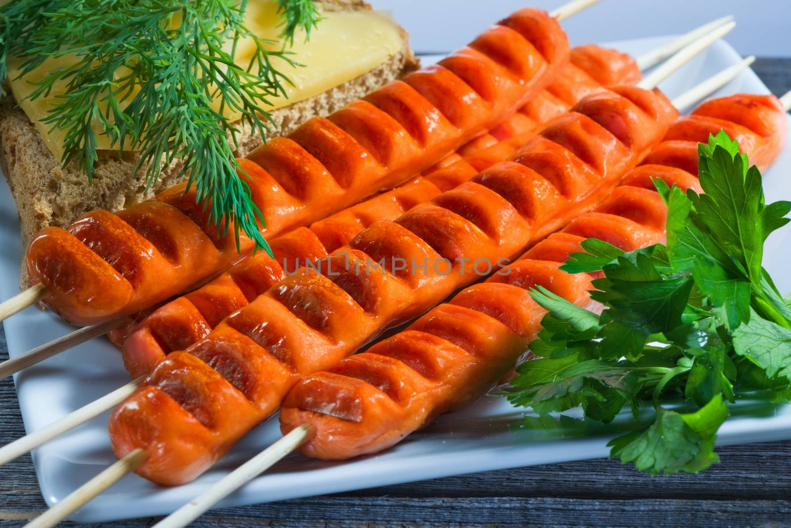 The sausages made on a grill, bread with cheese and greens on a rectangular plate