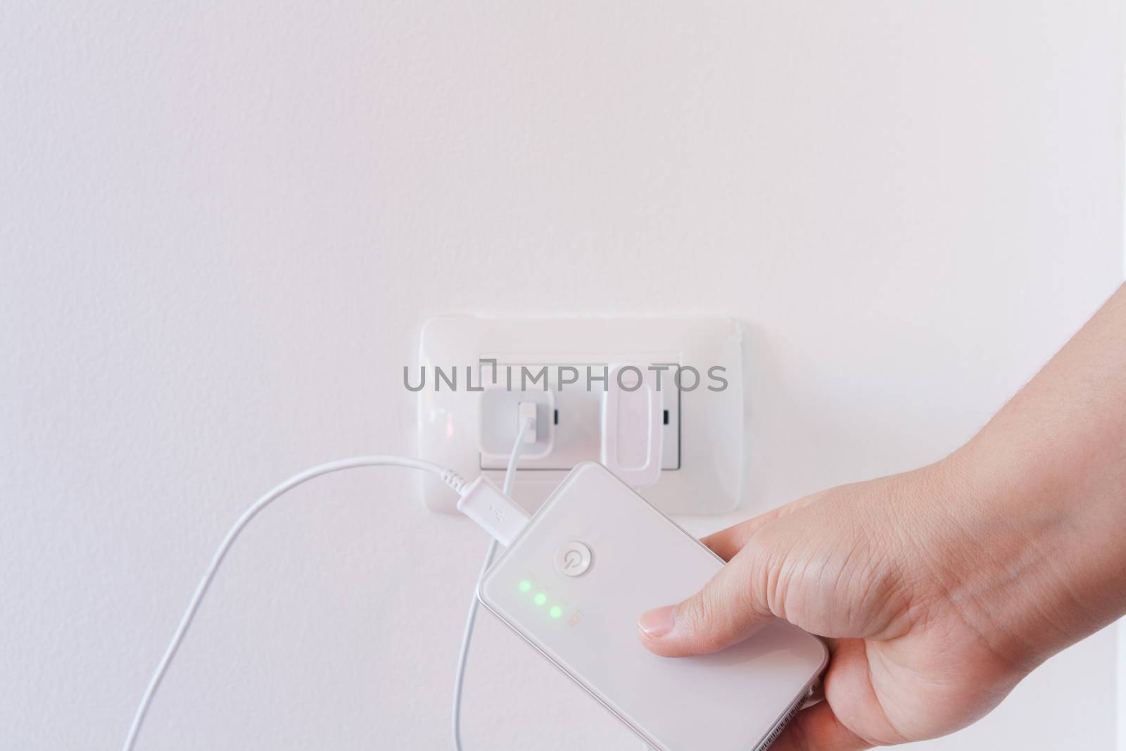 female hand plugging in the wall electtric plug of her power bank in a socket