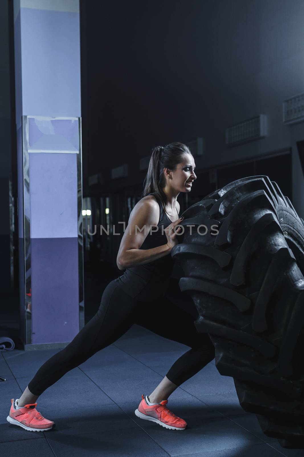 Powerful muscular woman CrossFit trainer doing tire workout at gym by mrakor