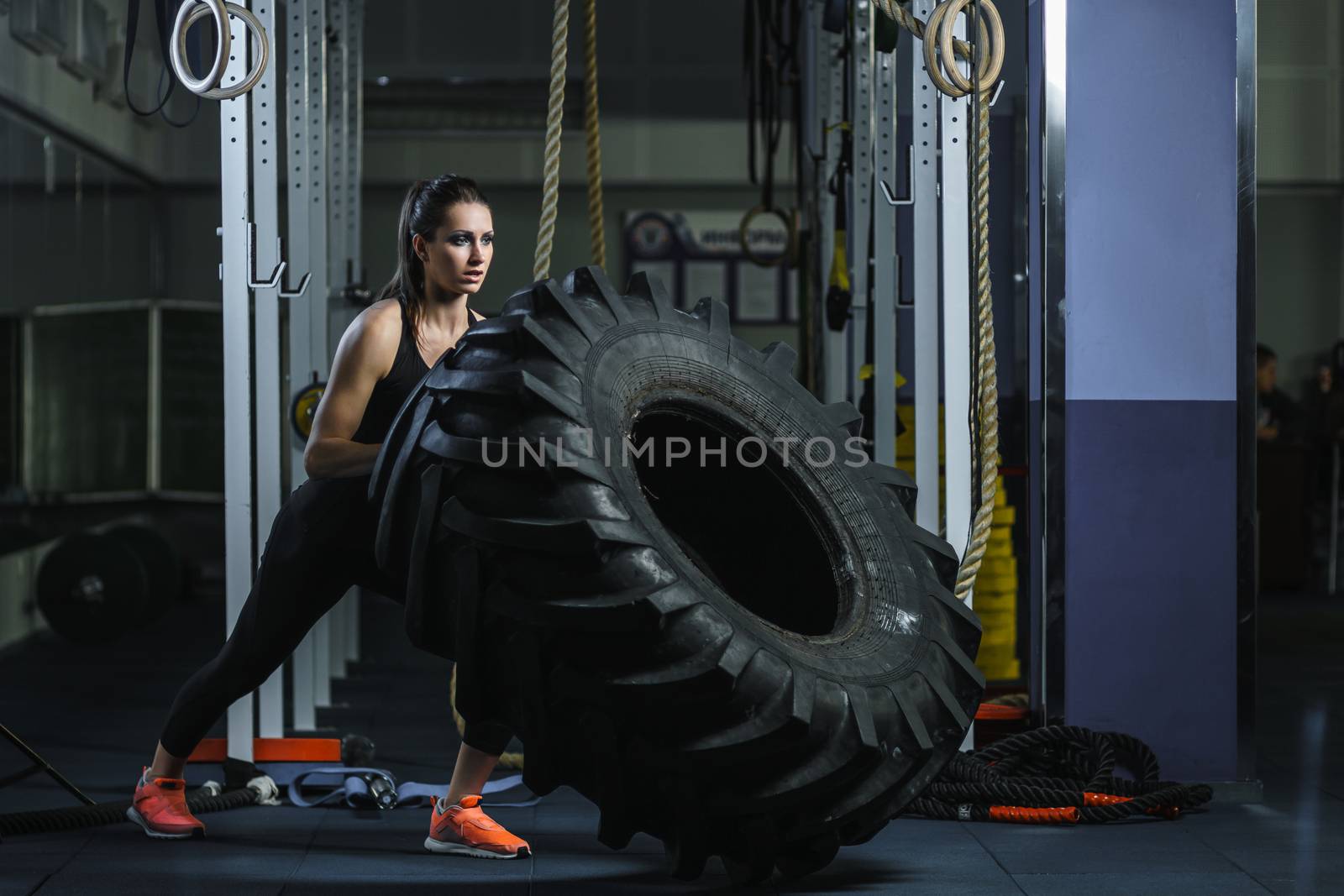 Concept: power, strength, healthy lifestyle, sport. Powerful attractive muscular woman CrossFit trainer doing giant tire workout at the gym