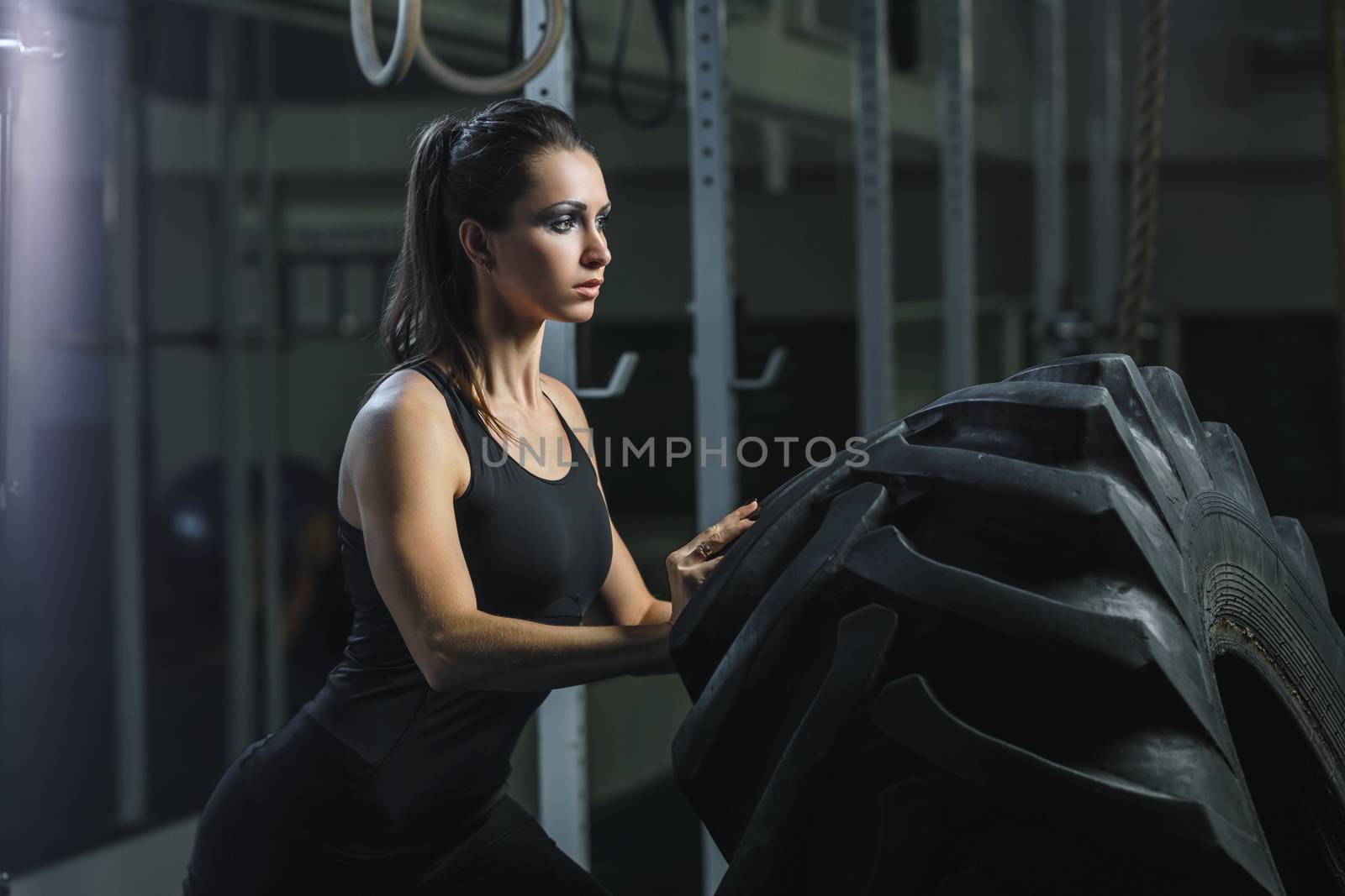 Concept: power, strength, healthy lifestyle, sport. Powerful attractive muscular woman CrossFit trainer doing giant tire workout at the gym