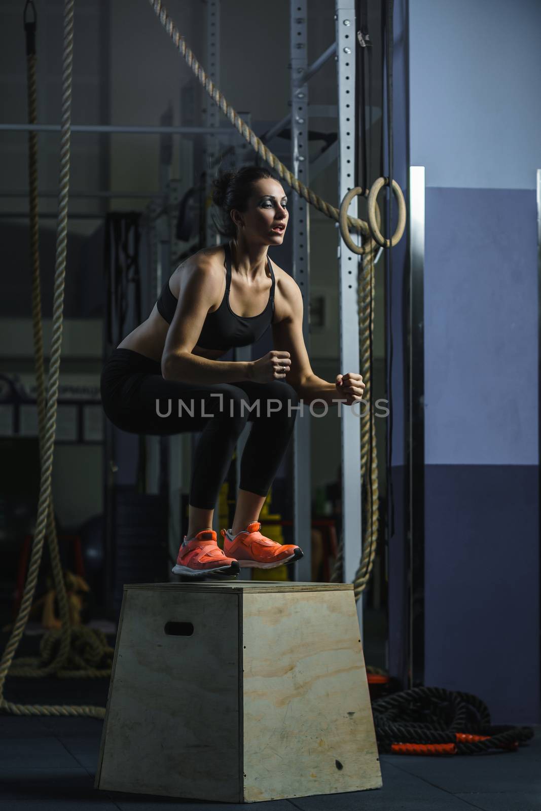 Powerful muscular woman CrossFit trainer jumps during workout at gym by mrakor