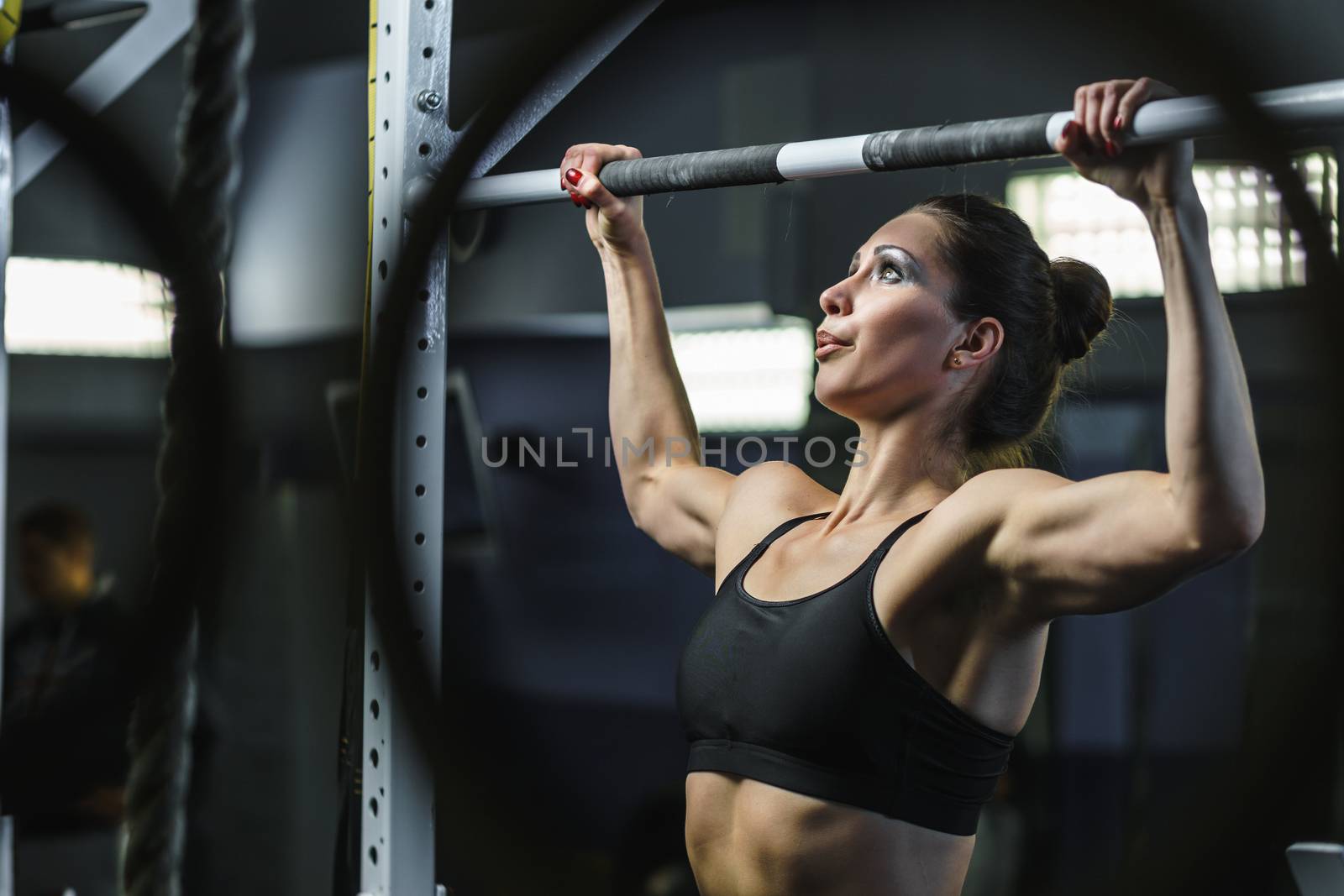 Powerful attractive woman CrossFit trainer do pull ups during workout by mrakor