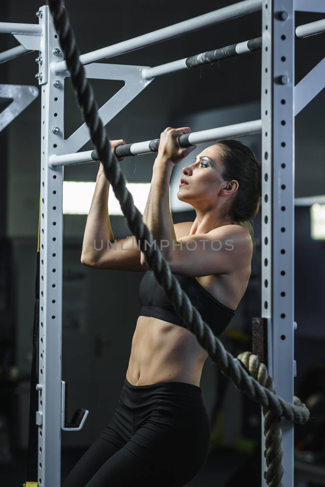 Powerful attractive woman CrossFit trainer do pull ups during workout by mrakor