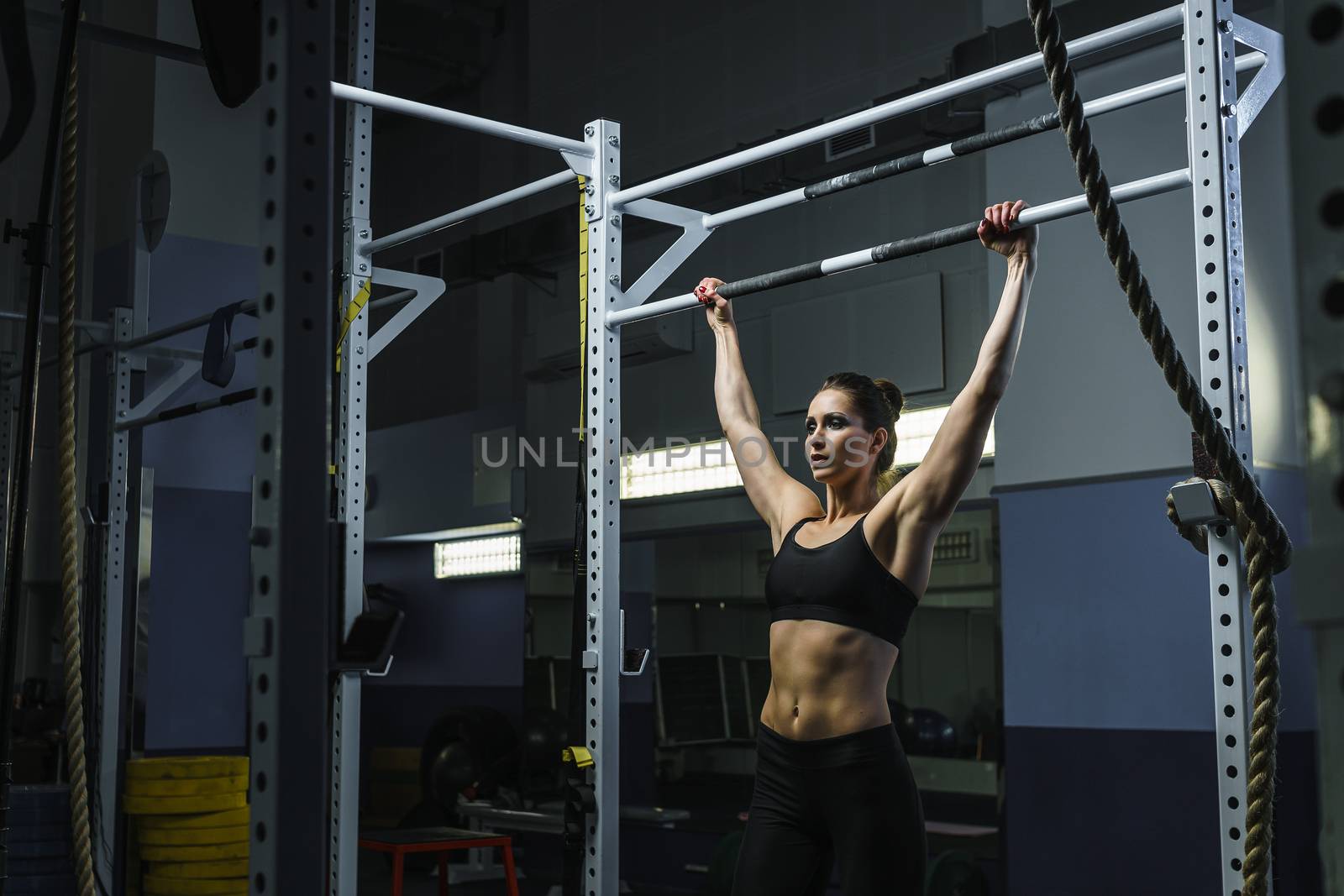 Powerful attractive woman CrossFit trainer do pull ups during workout by mrakor