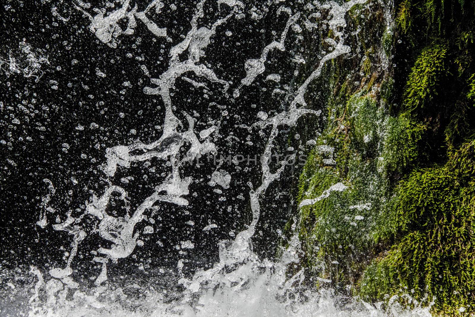 Fresh sparkling water falling over green moss of a waterfall. Horizontal image.