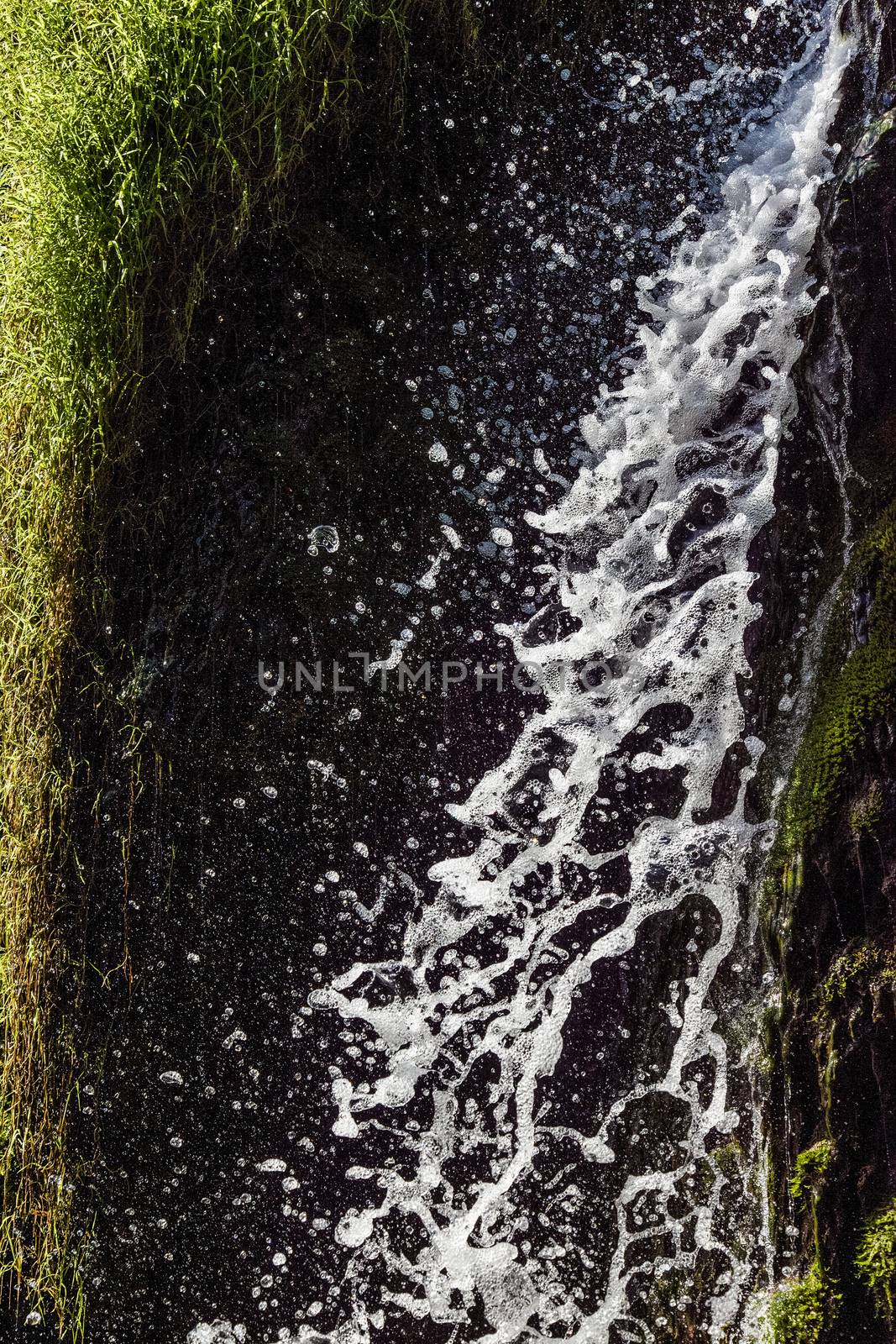 Fresh sparkling water falling over green moss of a beautiful waterfall. Vertical image.