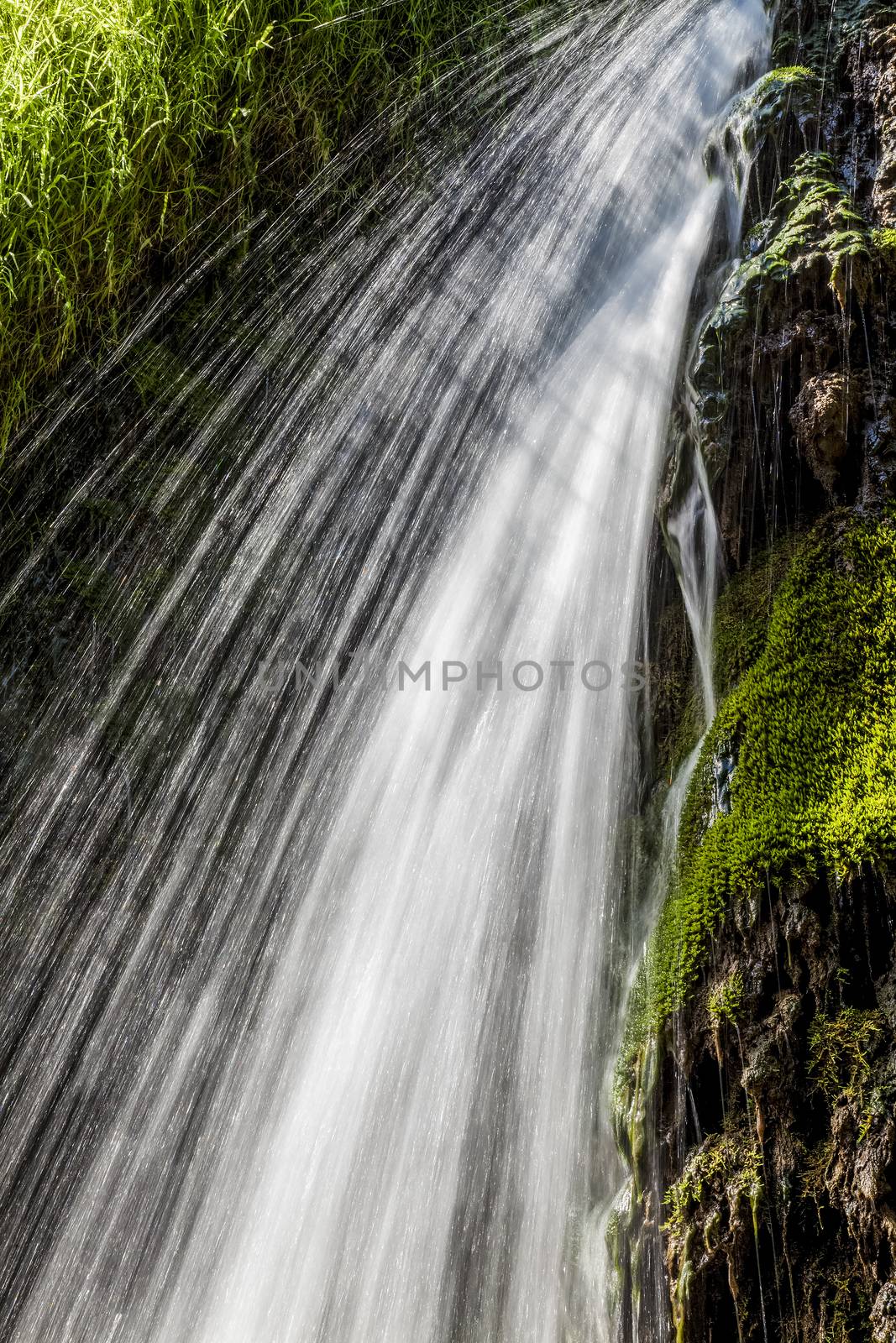 Movement blurred water falling over the moss of a waterfall. Vertical image.