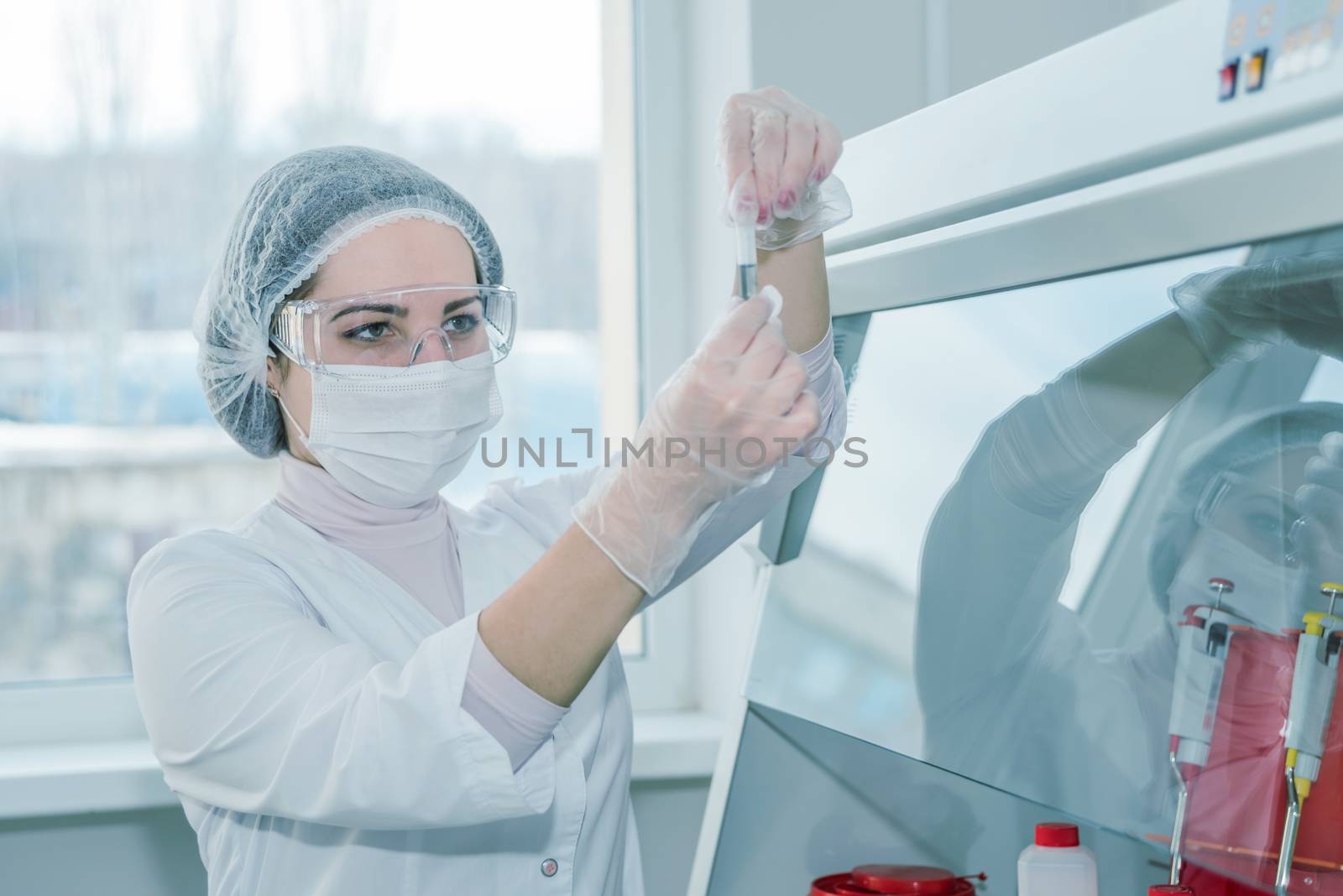 Woman scientist in a white protective clothing conducts research in a real lab