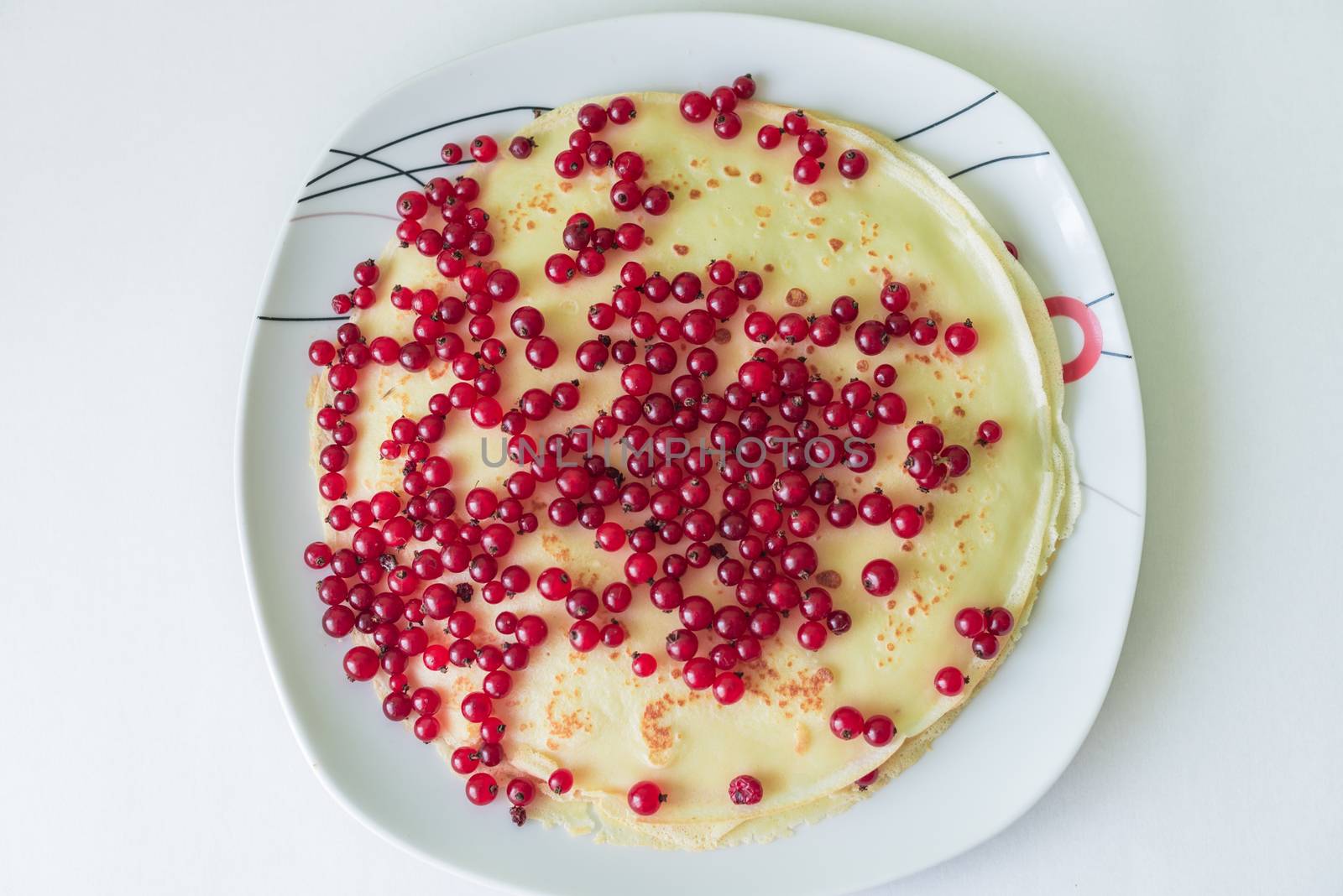 Pancakes with red currant berries in the plate on a white background