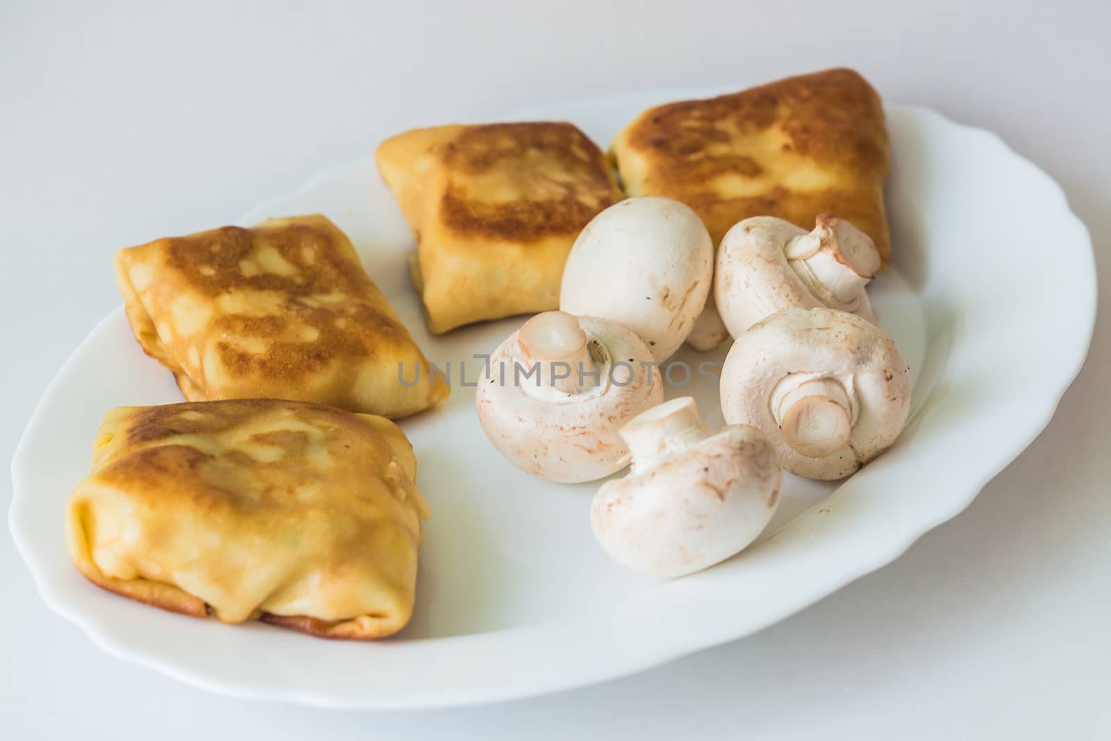 Fried pancakes with fillings and mushrooms in the white plate on a white background