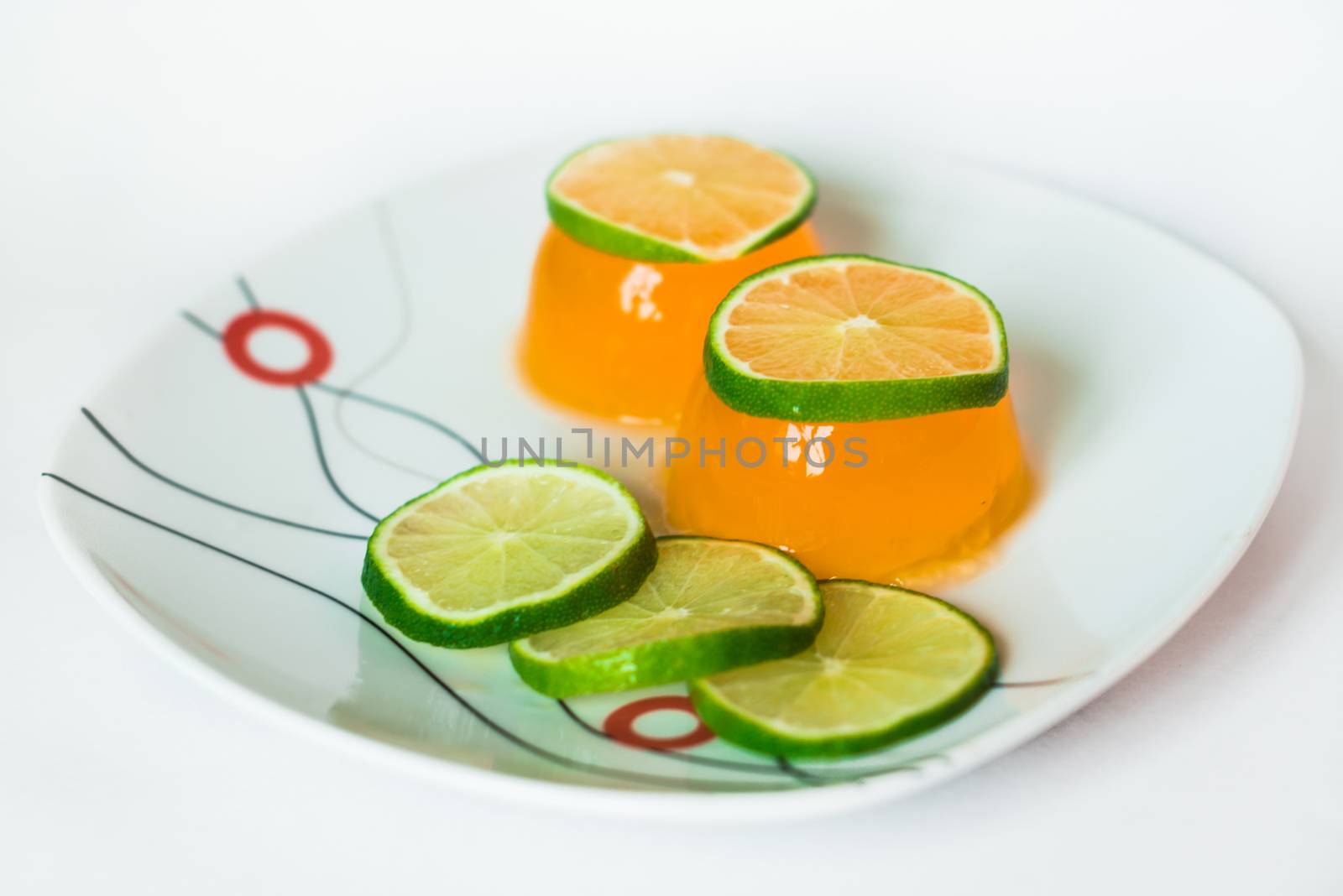 Orange jelly with slices of lime in a white plate on a white background