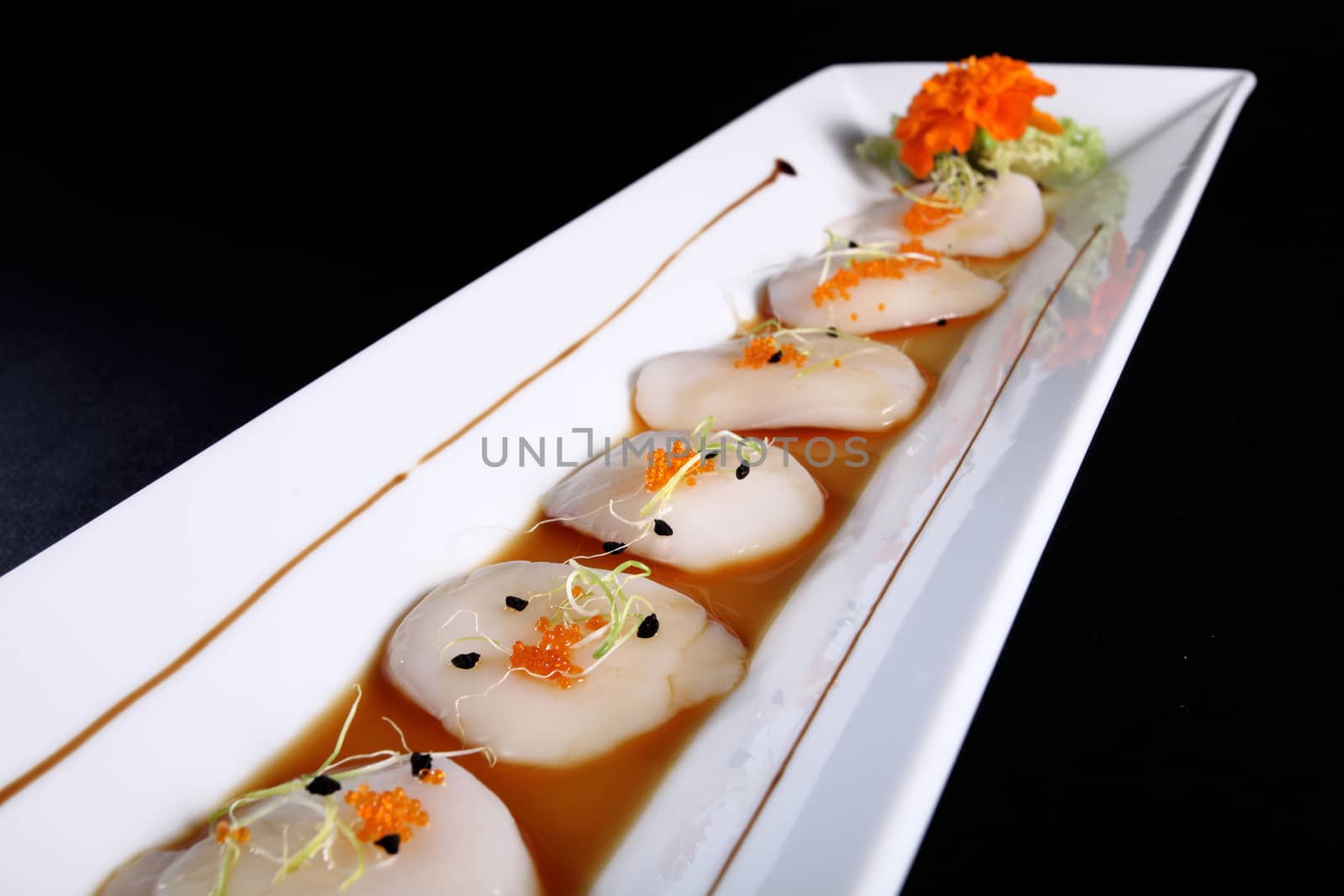 diced scallops with sauce on rectangular white plate, black background