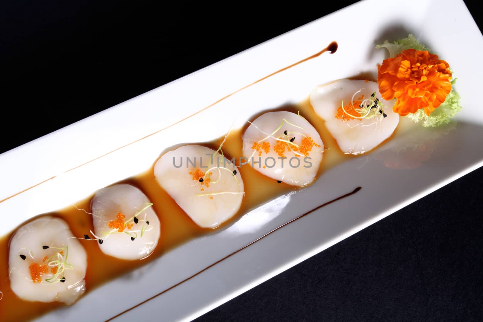 diced scallops with sauce on rectangular white plate, black background