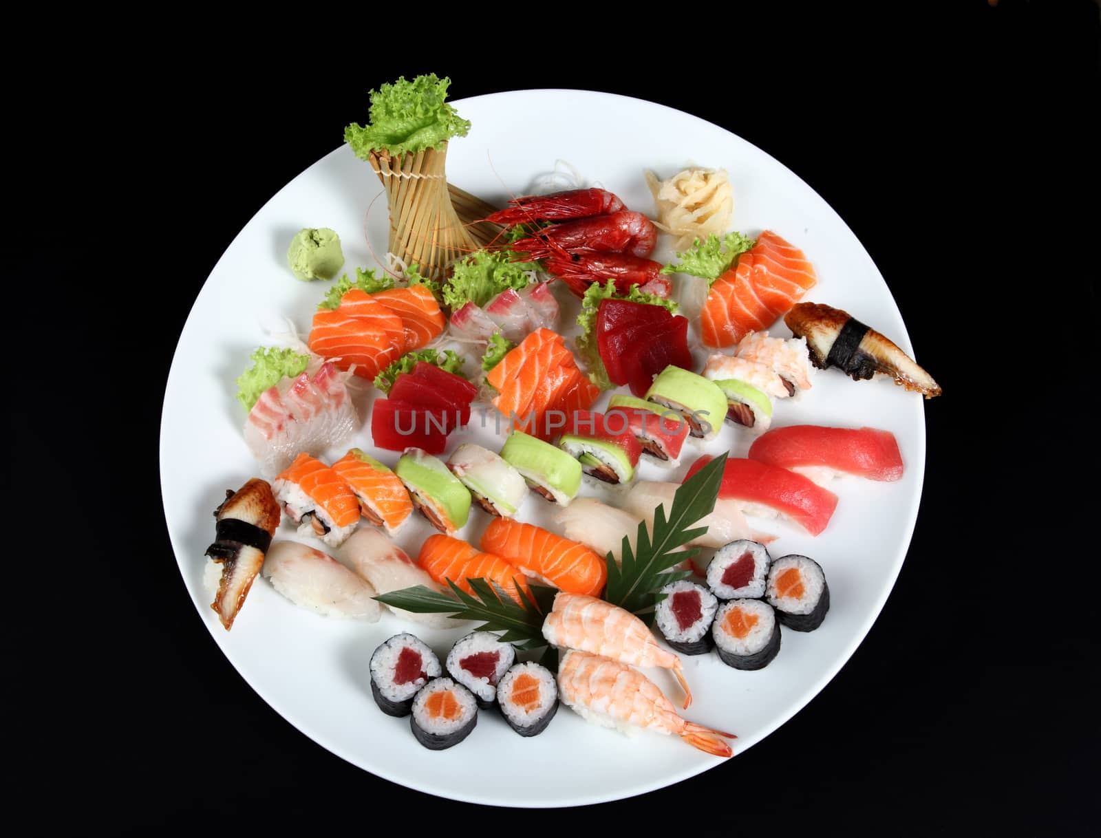sushi and sashimi mixed on round white plate on a black background