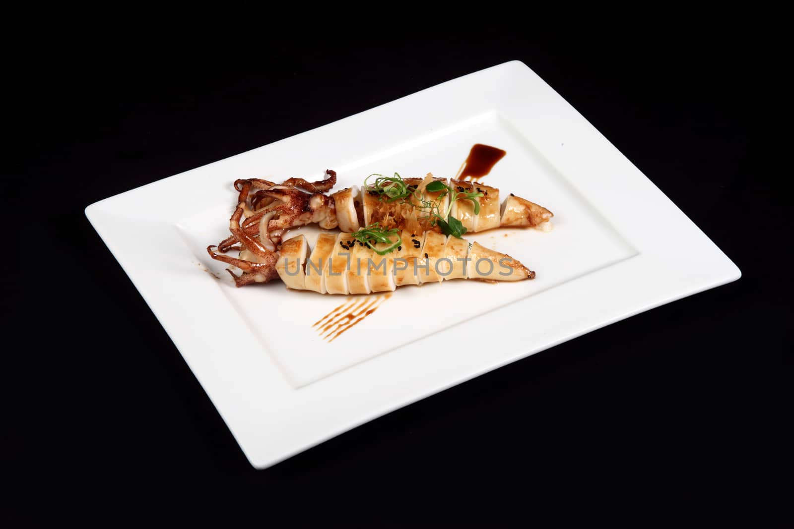 grilled squid with decoration of vegetables in white plate on a black background
