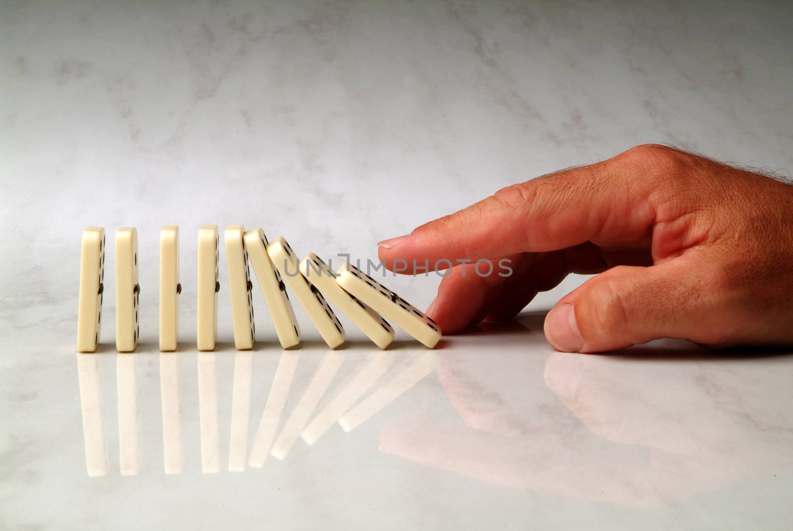 row of dominoes pushed by hand, on neutral background