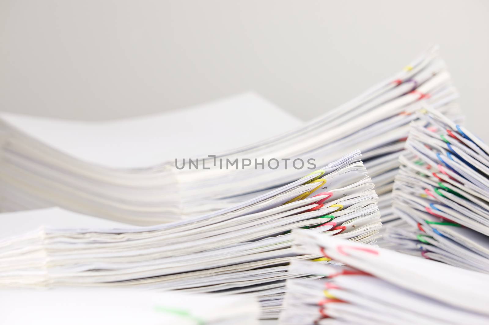 Pile overload paperwork of receipt and report with colorful paperclip have blur pile document foreground and background on white table.