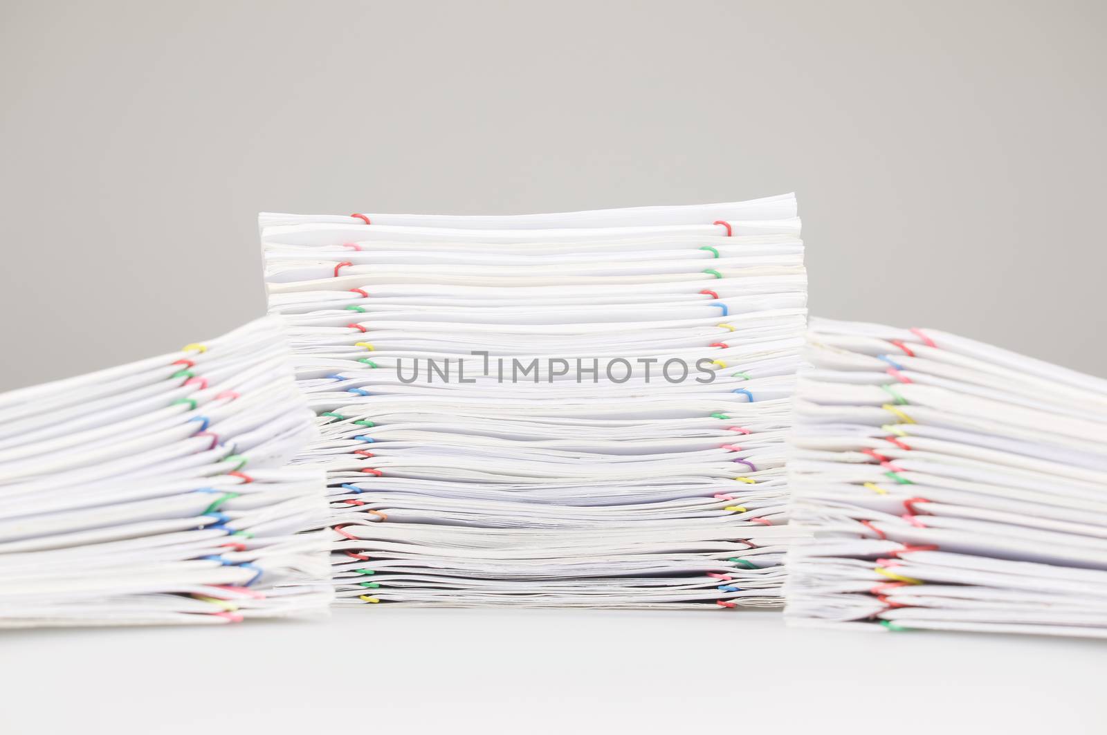 Pile overload paperwork of receipt and report with colorful paperclip have dual blur pile document foreground on white table.