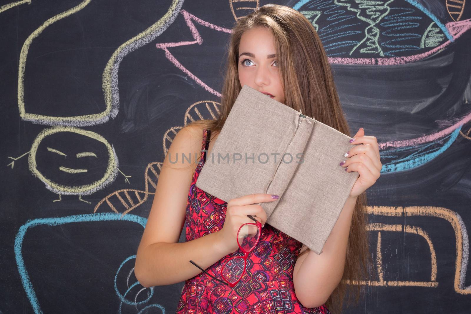 Perplexed  young student girl in red dress and red glasses reading a book hides behind it