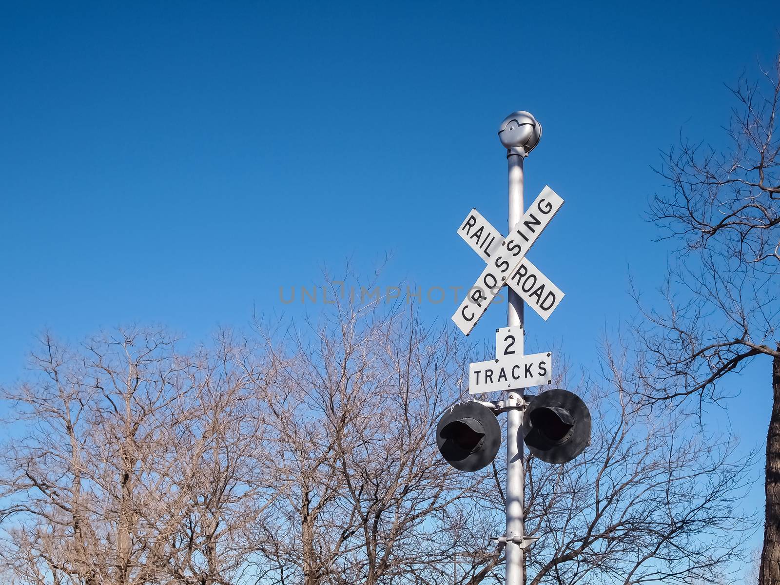 Railroad crossing sign against blue sky and tree background, with space for your text.