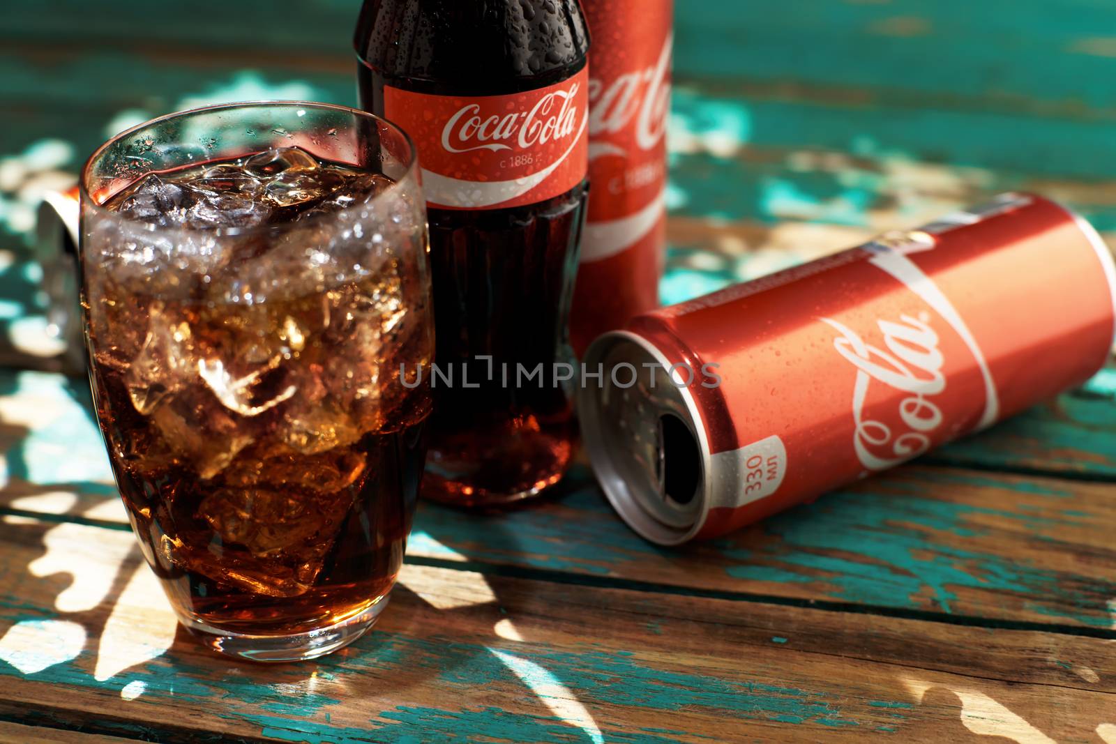 MINSK, BELARUS-AUGUST 25, 2016. Can and a glass of iced Coca-Cola on a wooden table by vmytra