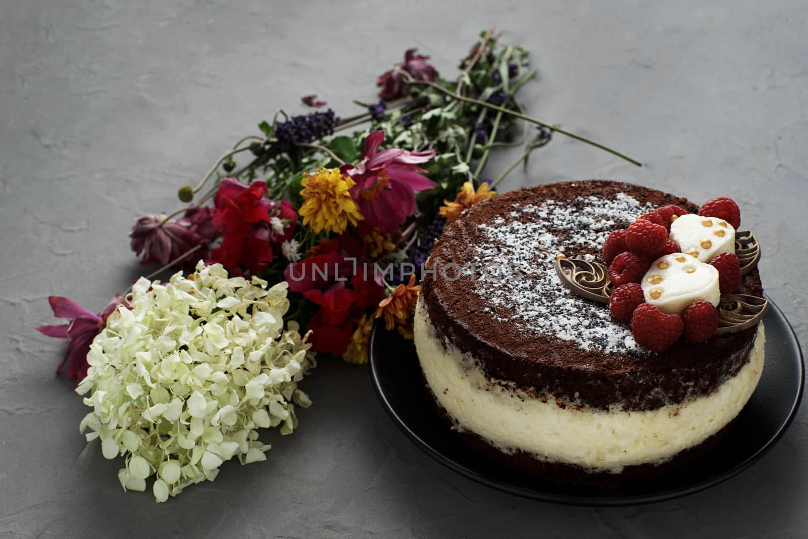 Cake covered with chocolate decorated raspberries, with a bouquet of flowers on a gray background. by vmytra