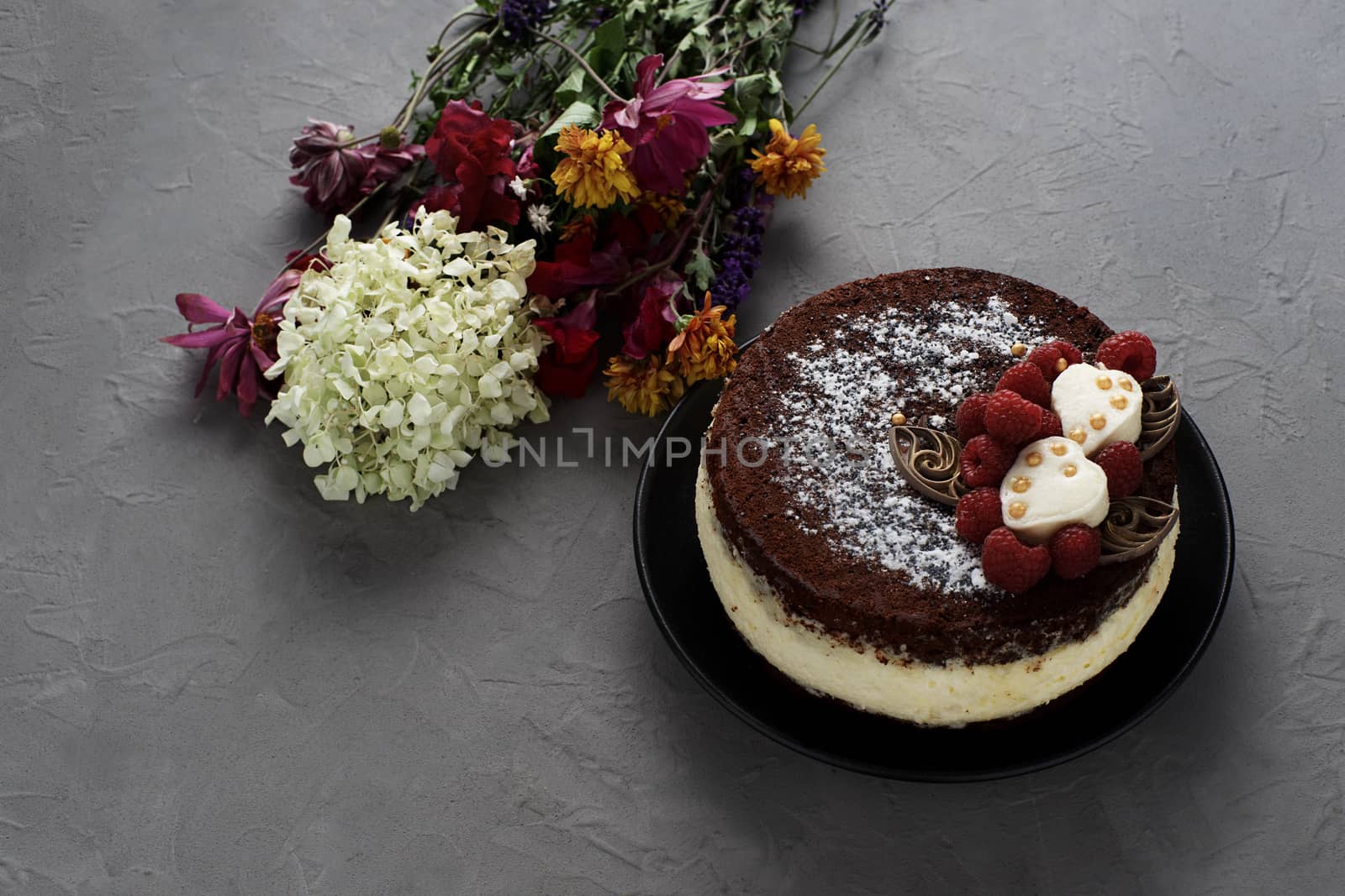 Cake covered with chocolate decorated raspberries, with a bouquet of flowers on a gray background. by vmytra