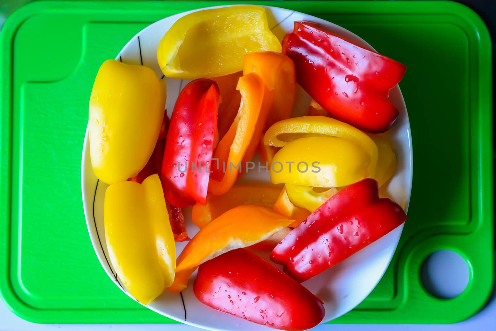 Slices of bell peppers in a white plate on the green plastic board
