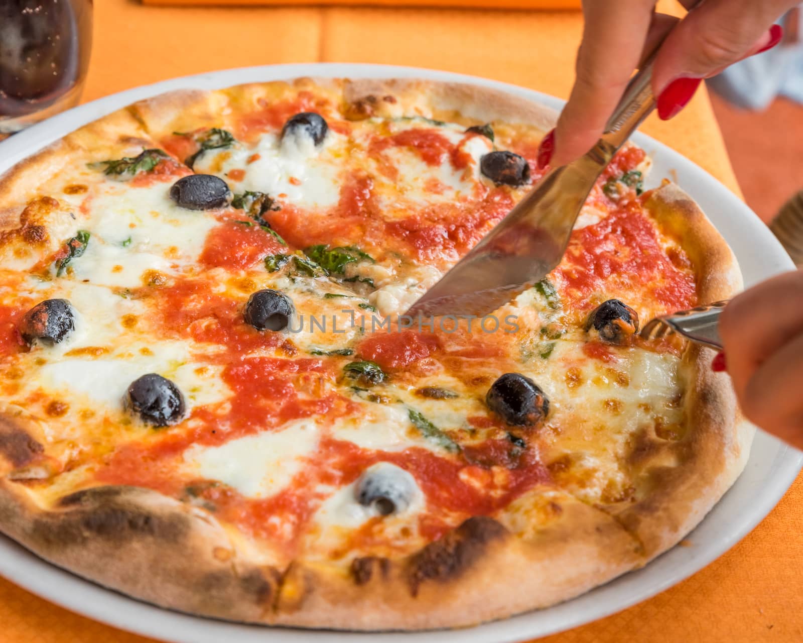 Close-up of woman hands cutting pizza outside at restaurant, selective focus.