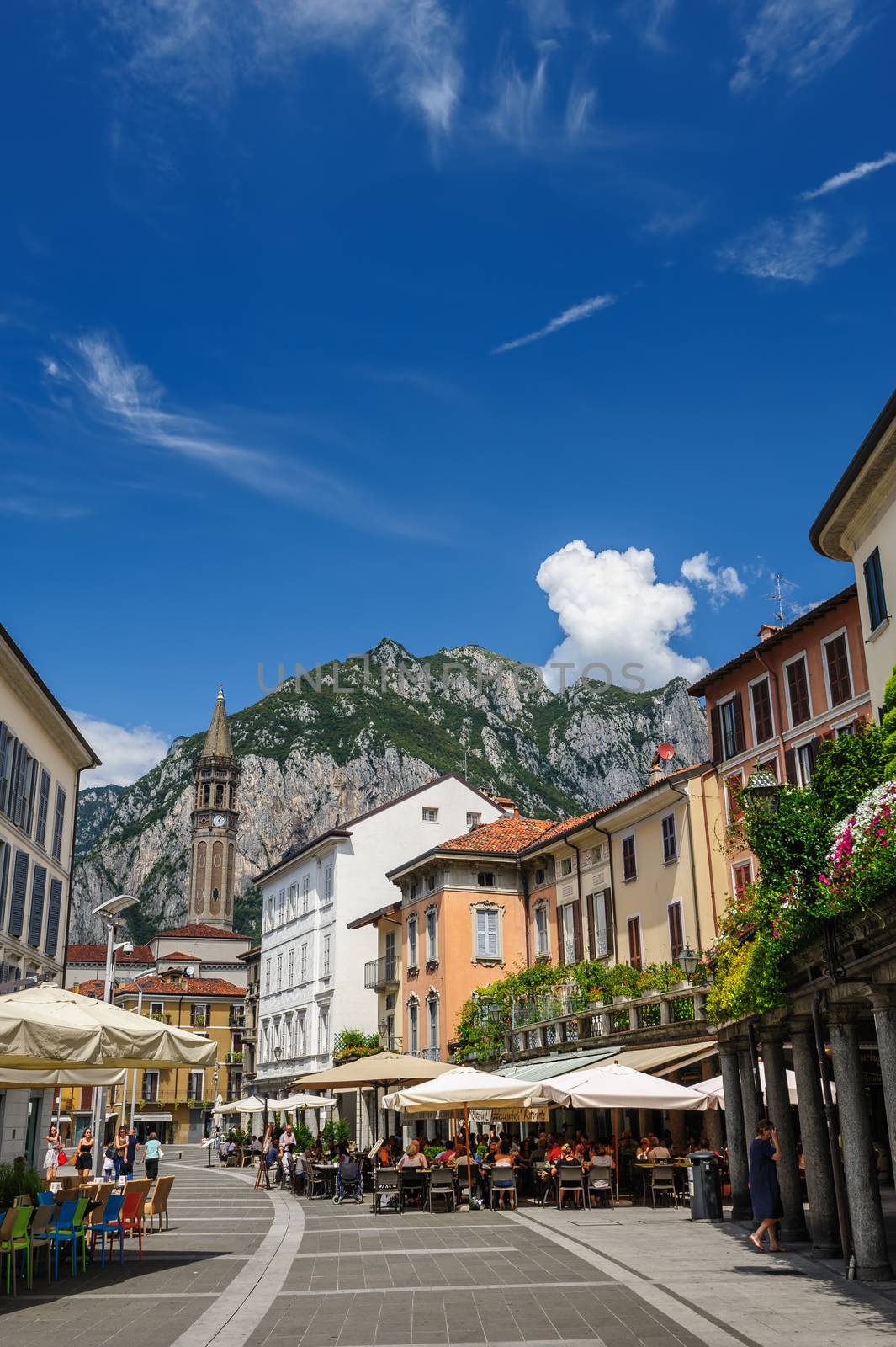 Lecco, Italy - August 17th, 2016: Central streets of Lecco town, with people relaxing in outdoor cafe and bell tower.