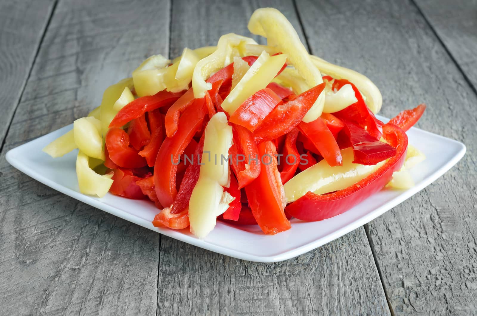 Chopped sweet pepper, white plate and wooden background.