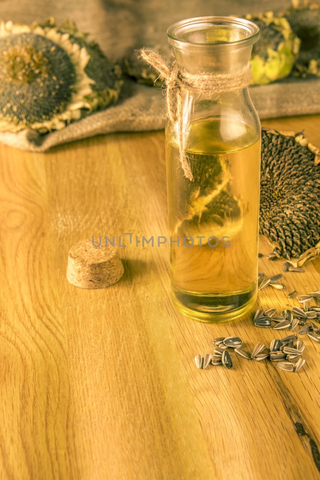 Bottle with cold pressed oil on a wooden table with sunflower plants and seeds all over it