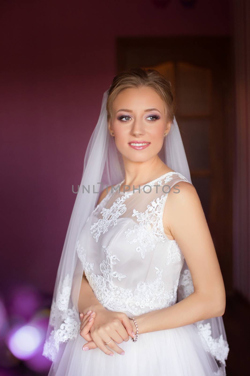 Portrait of beautiful bride with fashion veil posing on bed at wedding morning. Makeup. Brunette girl with long wavy hair styling. Wedding dress.