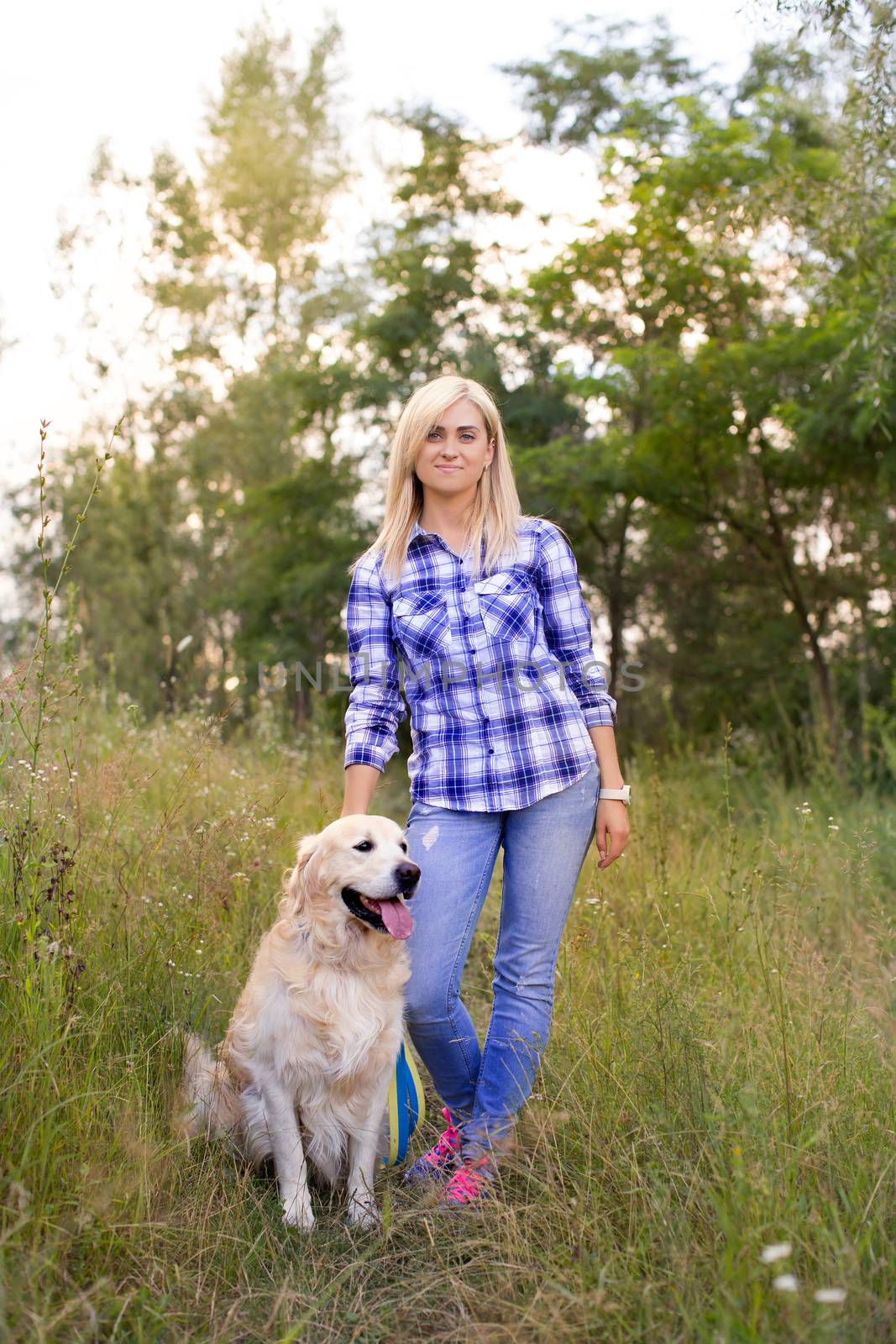 Girl walking with a dog on a green meadow