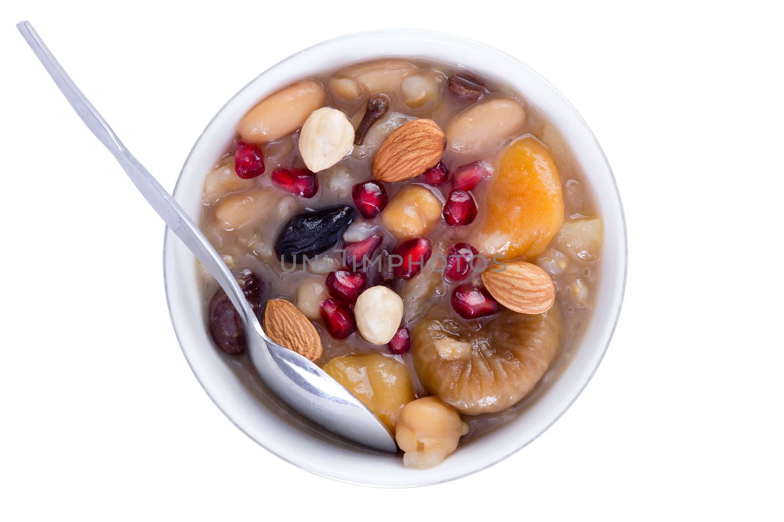 Colorful healthy Noah's Pudding or Turkish ashure, a sweet grain dessert, served with pomegranate seeds, almonds and hazel nuts in a white bowl with silver spoon, viewed from above isolated on white