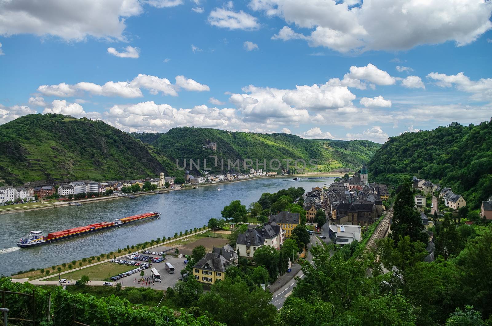 Panoramic view of Sank-Goar and Snak Goarshausen medival village and Rhine vineyards on slope of the hills in Germany. Cargo ship sails on the Rhine river.