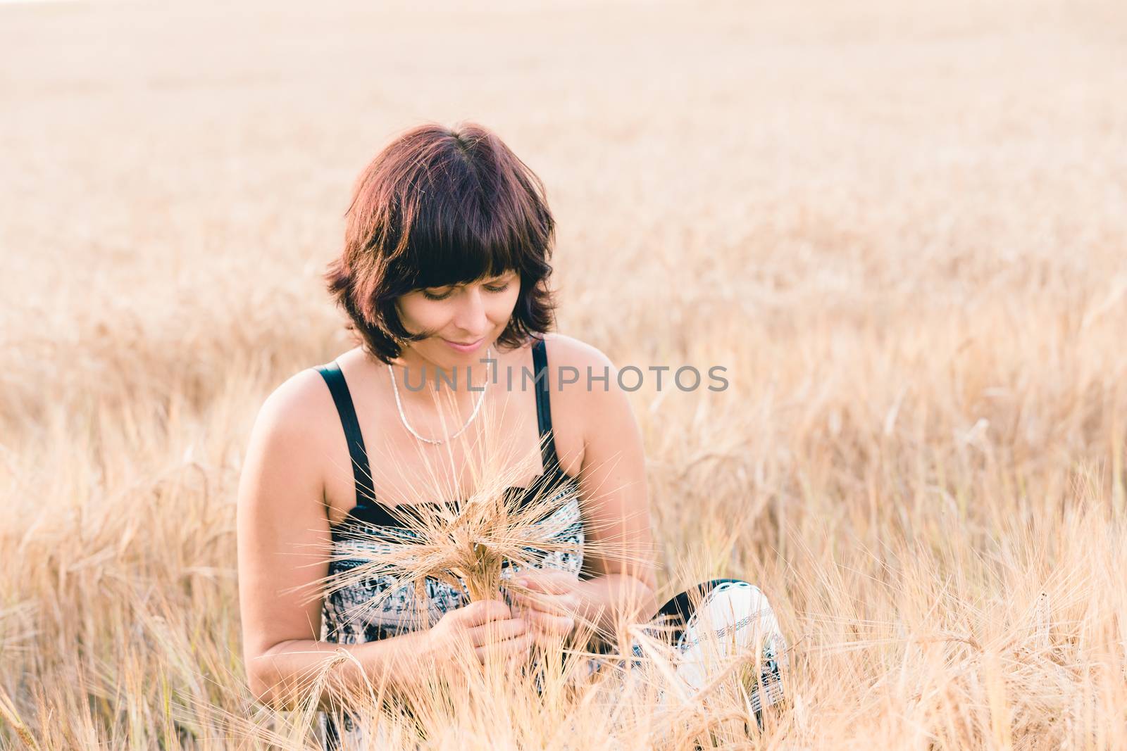 Middle aged beauty woman with summer dress and no makeup relaxing in countryside tearing into bouquet of golden barley with her hand, summer concept