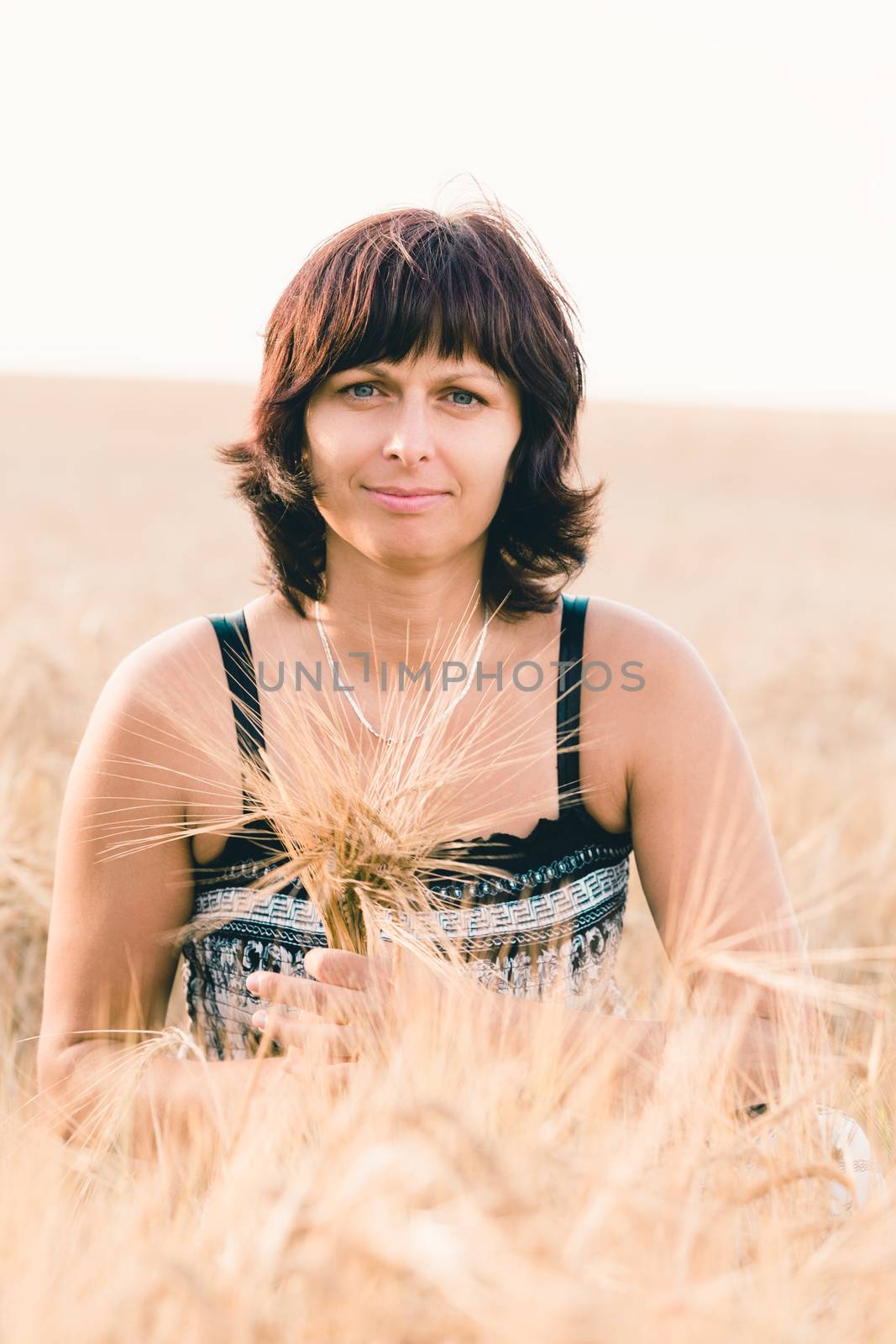 Middle aged beauty woman with summer dress and no makeup relaxing in countryside tearing into bouquet of golden barley with her hand, summer concept