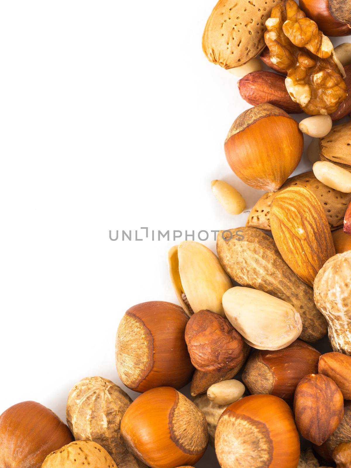 Background of mixed nuts - hazelnuts, almonds, walnuts, pistachios, peanuts, pine nuts peeled and not peeled - vertical with copy space. Isolated one edge. Top view or flat lay