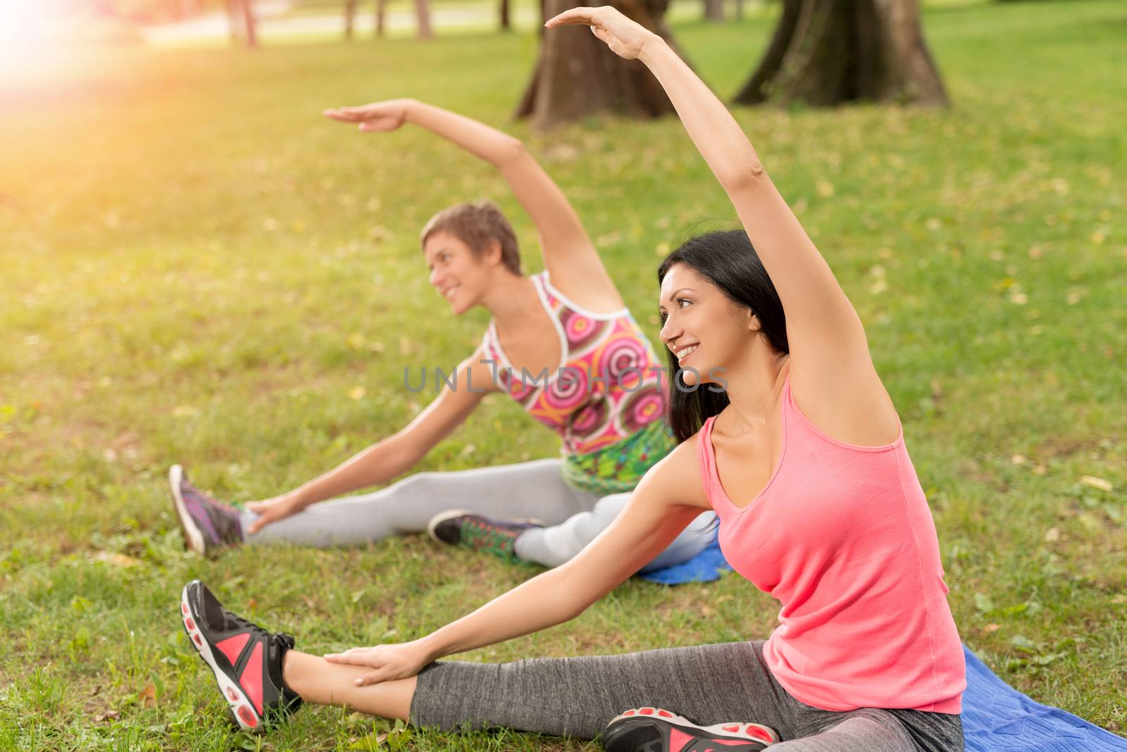 Two beautiful women doing stretching exercise in the park. 