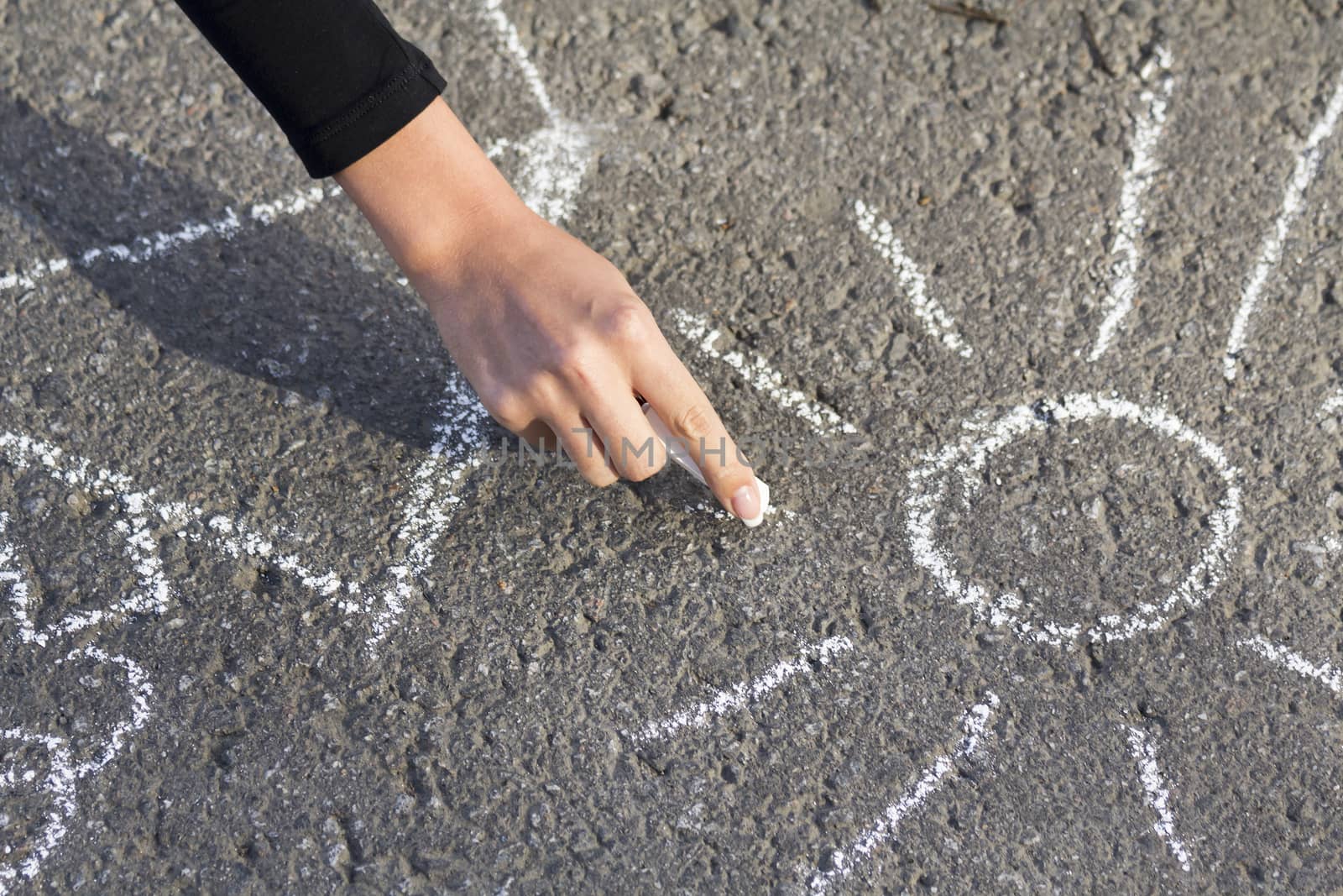 Hand girl draws by a chalk picture House and the Sun on asphalt in the summer outdoors