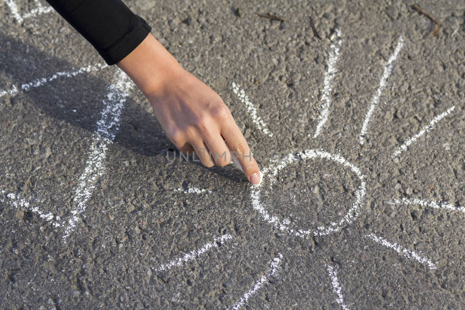 Hand girl draws by a chalk picture House and the Sun on asphalt in the great outdoors