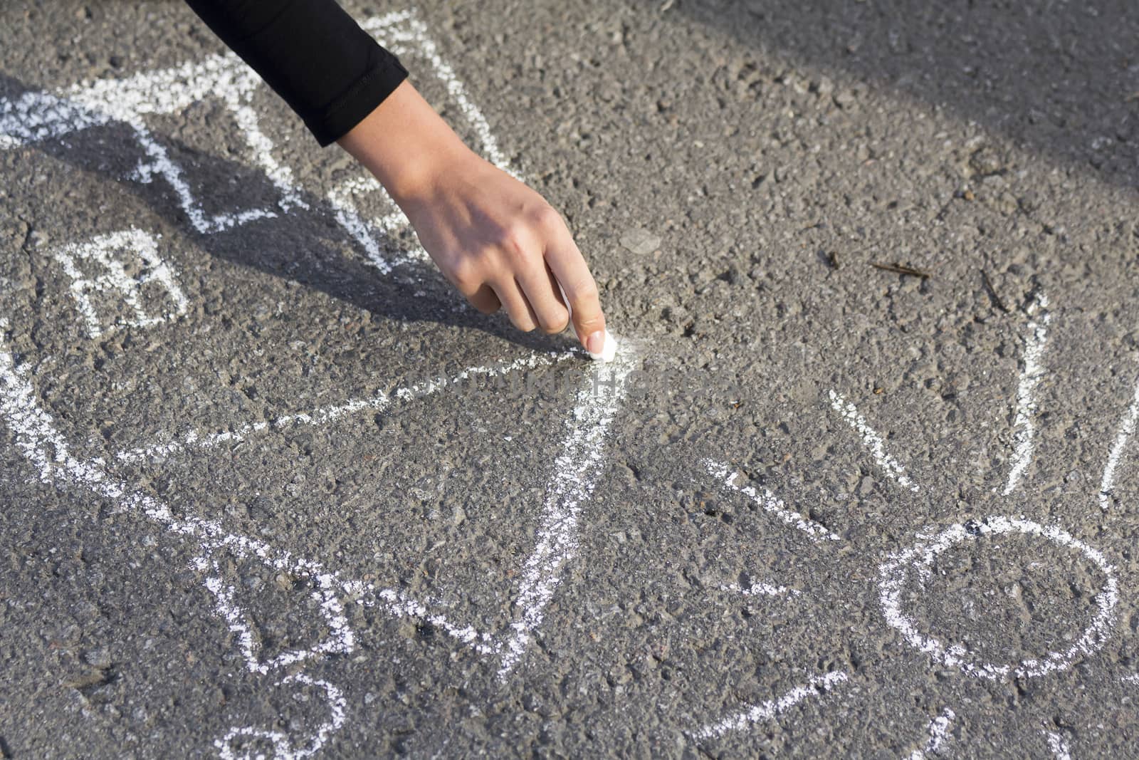 Hand girl draws by a chalk picture House and the Sun on asphalt