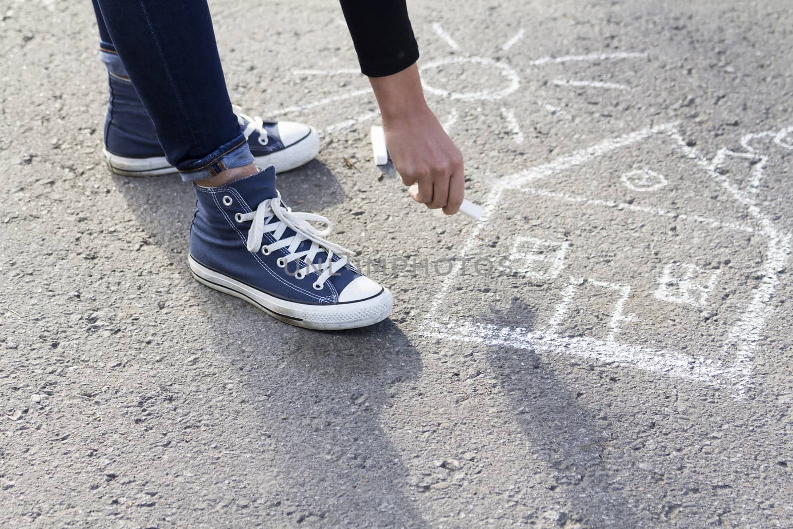 Girl draws by a chalk picture House and the Sun on asphalt