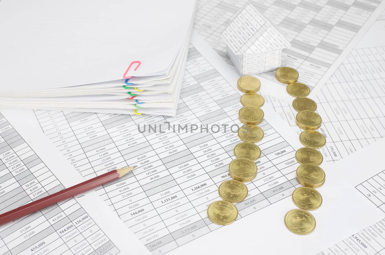 Pile of gold coins place as way to home on finance account have pencil and blur pile overload paperwork of report and receipt with colorful paperclip as background.