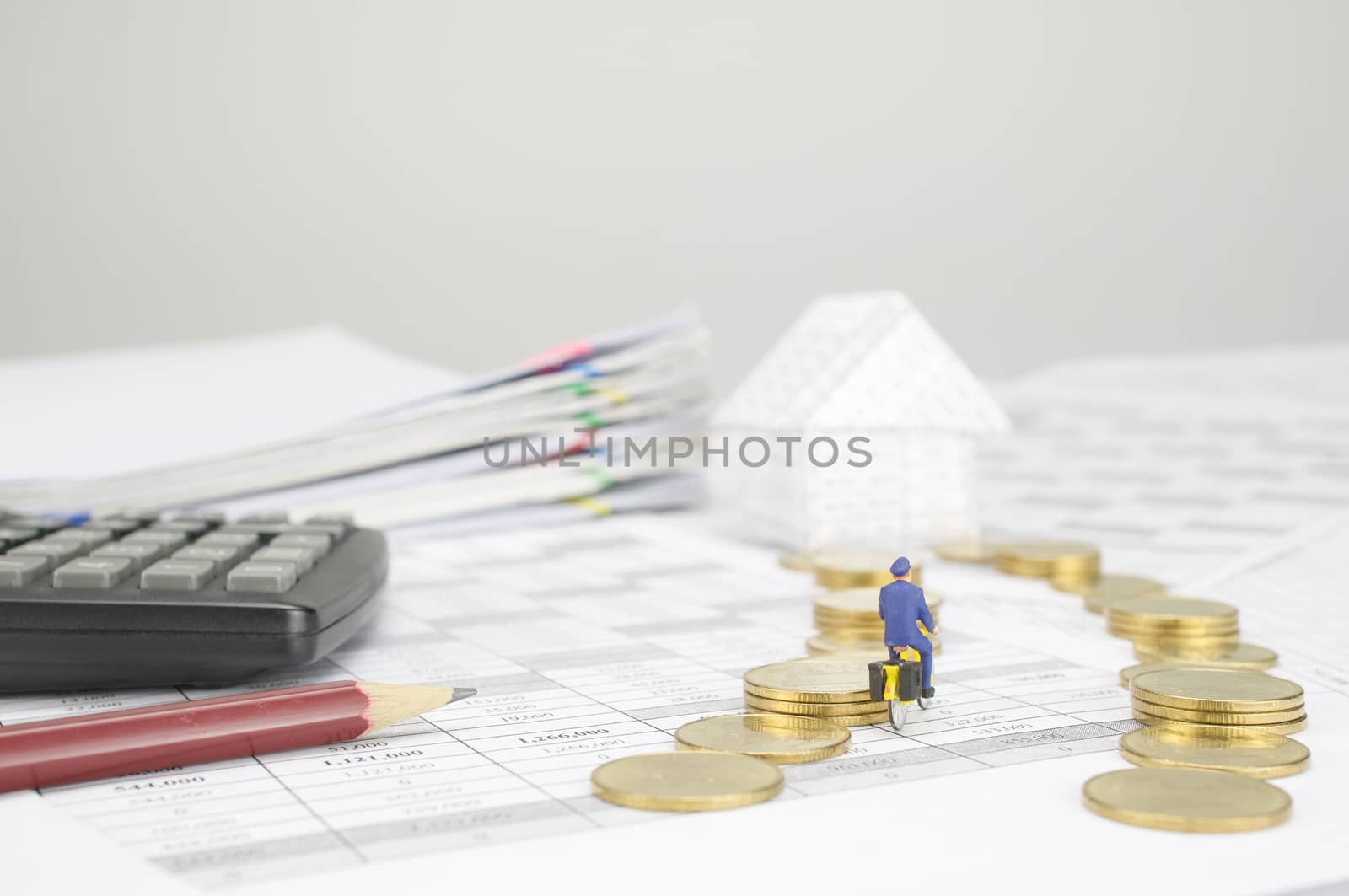 Postman is cycling pass step pile of gold coins to house on finance account have pencil with blur calculator and pile overload paperwork of report and receipt with colorful paperclip as background.