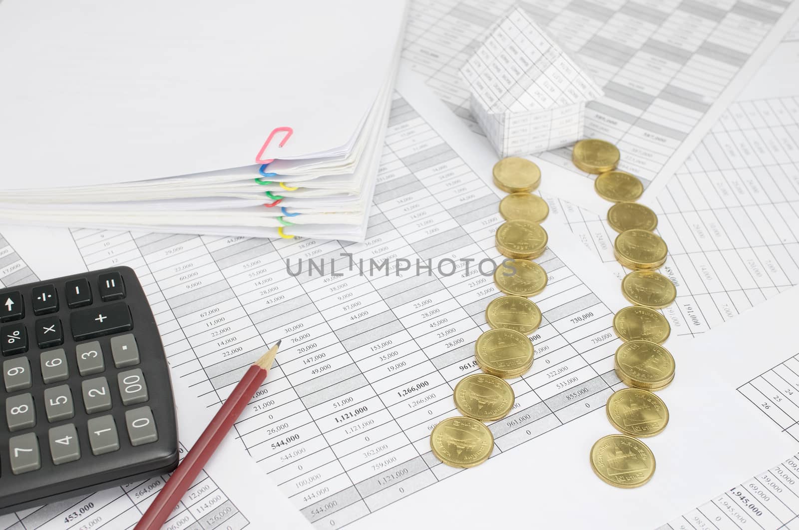 Pile of gold coins place as way to house on finance account have pencil with calculator and blur pile overload paperwork of report and receipt with colorful paperclip as background.