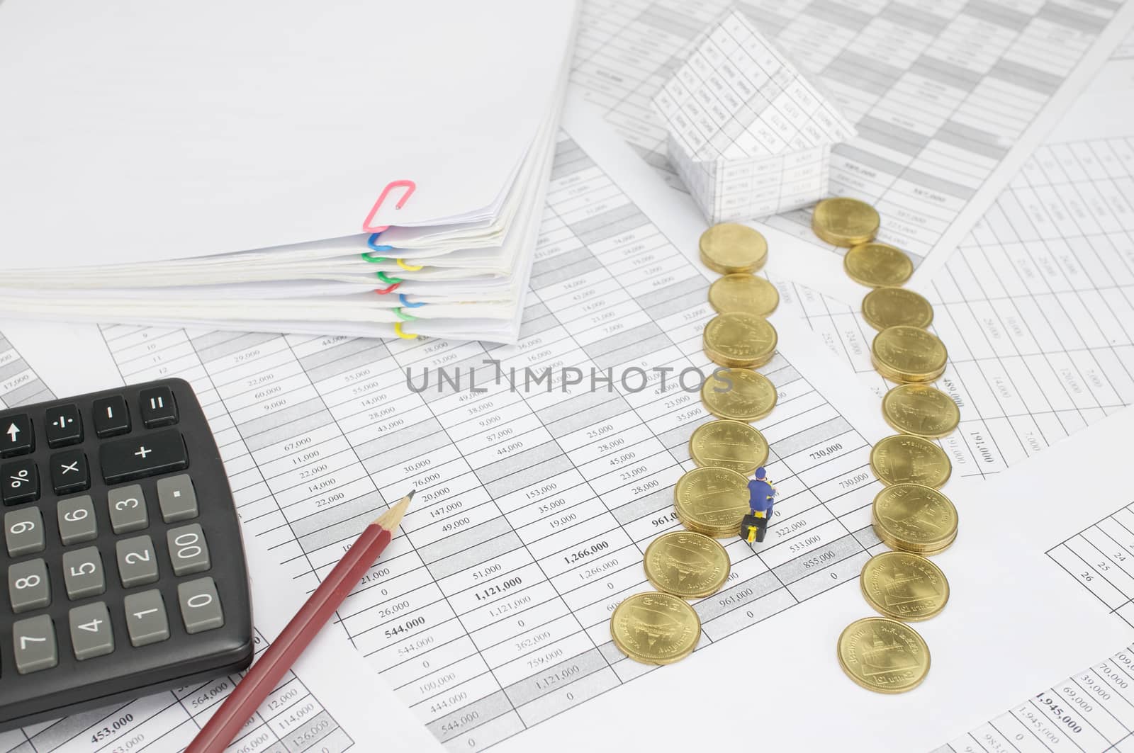 Postman is cycling pass step pile of gold coins to house on finance account have pencil with calculator and blur pile overload paperwork of report and receipt with colorful paperclip as background.